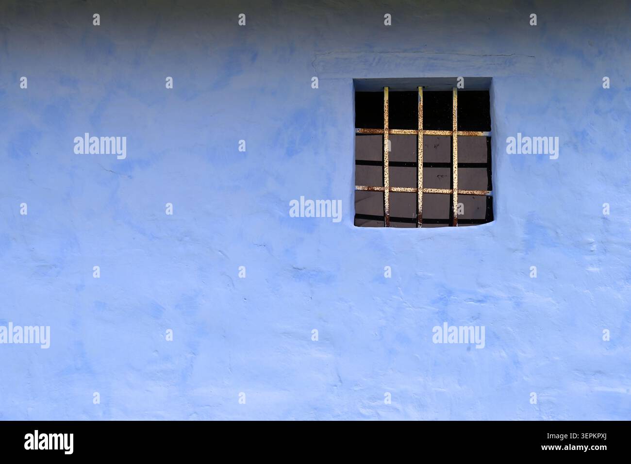 Pareti in stucco blu rustico con piccola finestra sbarrata e barre di ferro intemprate Foto Stock