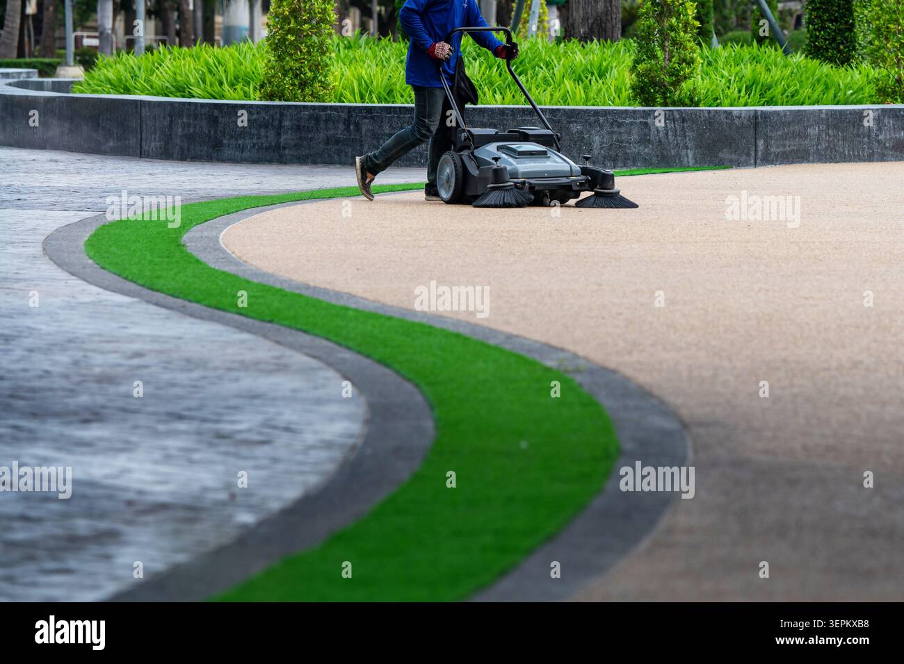 Un addetto alla manutenzione che utilizza una macchina per il prato per rifinire il percorso di un parco pubblico, mostrando la pulizia e la cura del paesaggio all'aperto in uno spazio verde della comunità. Foto Stock