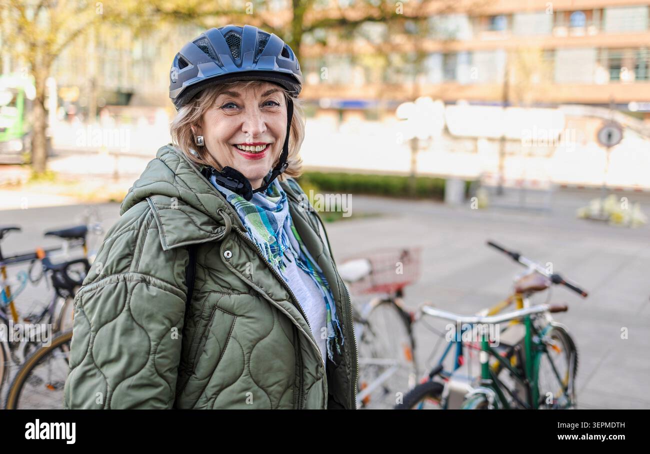 Donna anziana che indossa il casco mentre va in bicicletta in città Foto Stock