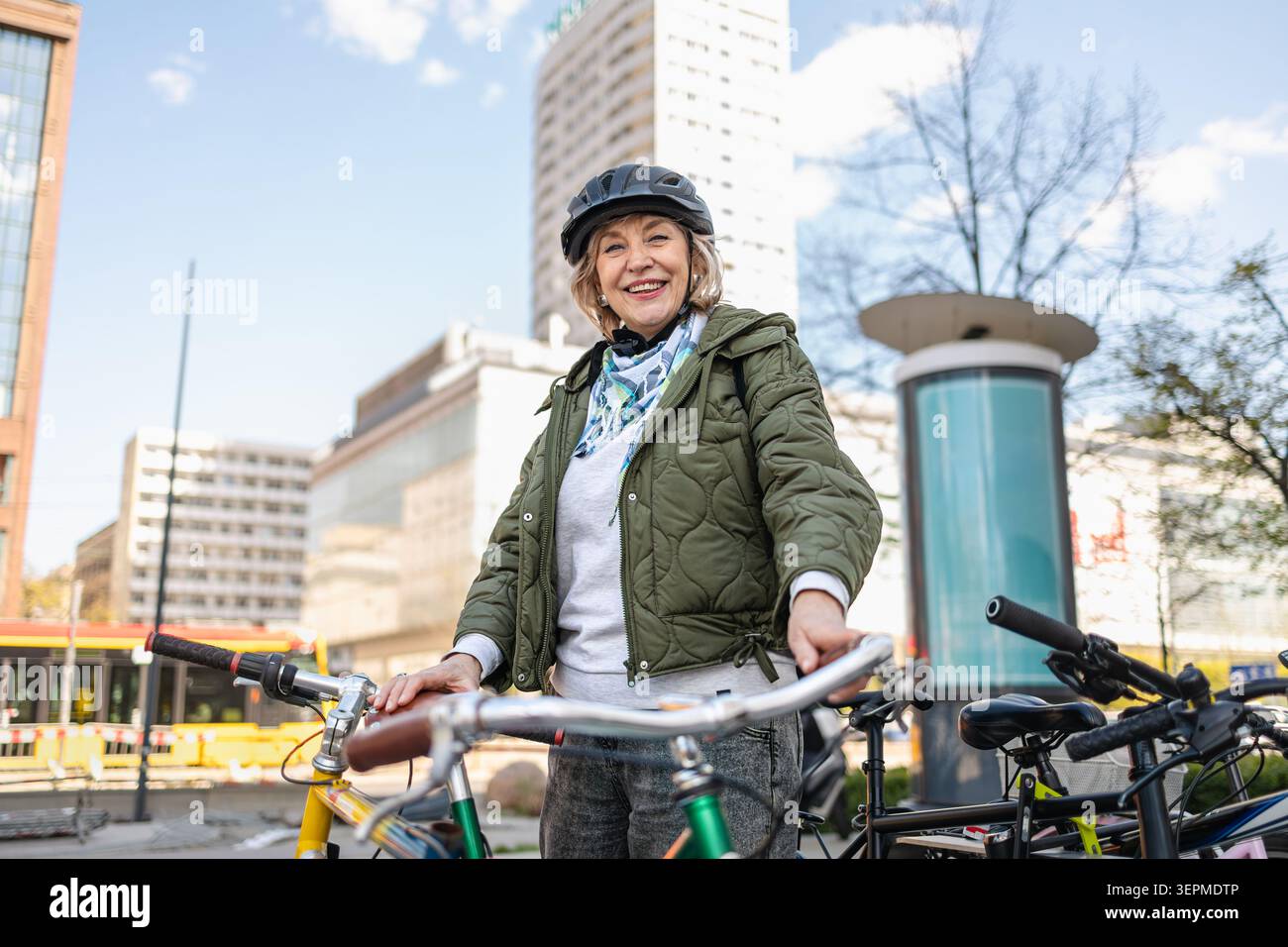 Donna anziana che indossa il casco mentre va in bicicletta in città Foto Stock