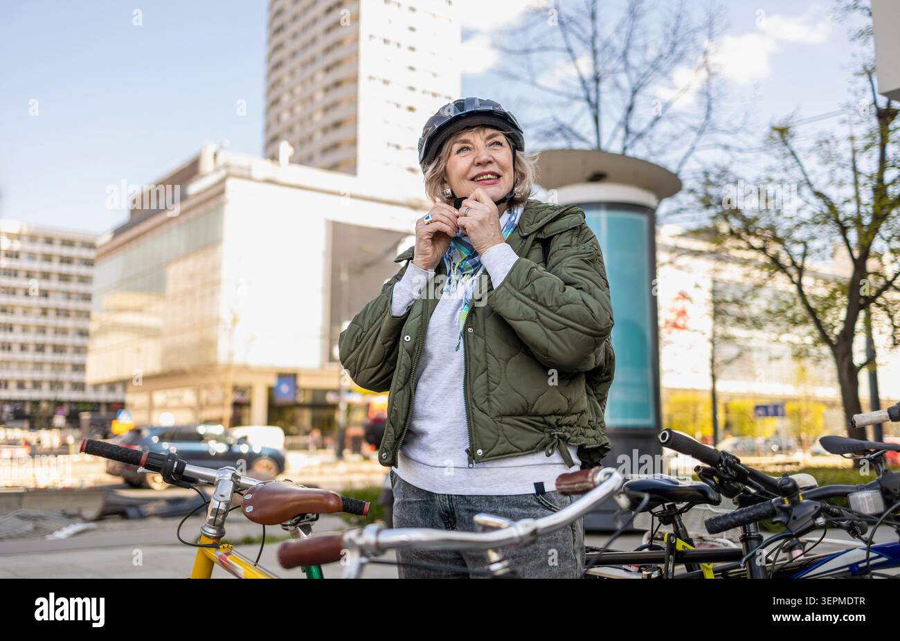 Donna anziana che indossa il casco mentre va in bicicletta in città Foto Stock