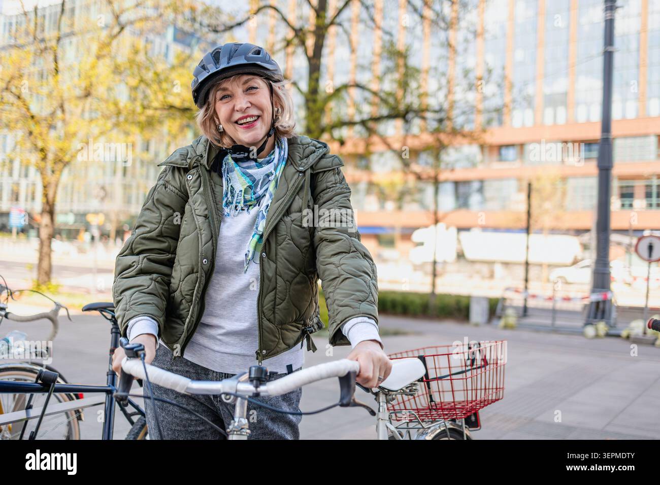 Donna anziana che indossa il casco mentre va in bicicletta in città Foto Stock