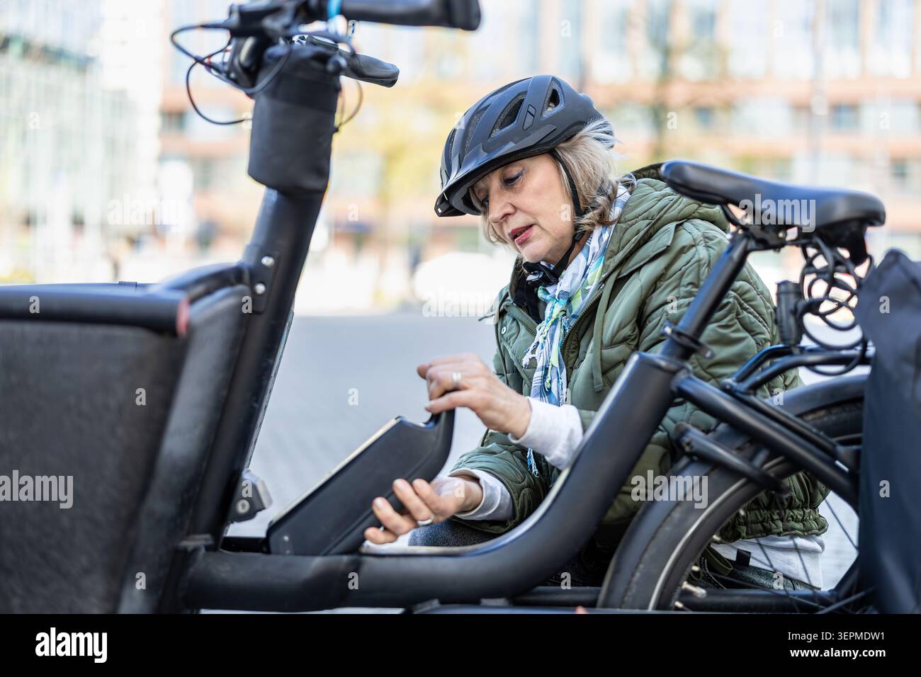 Donna matura che cambia la batteria su una bicicletta elettrica Foto Stock