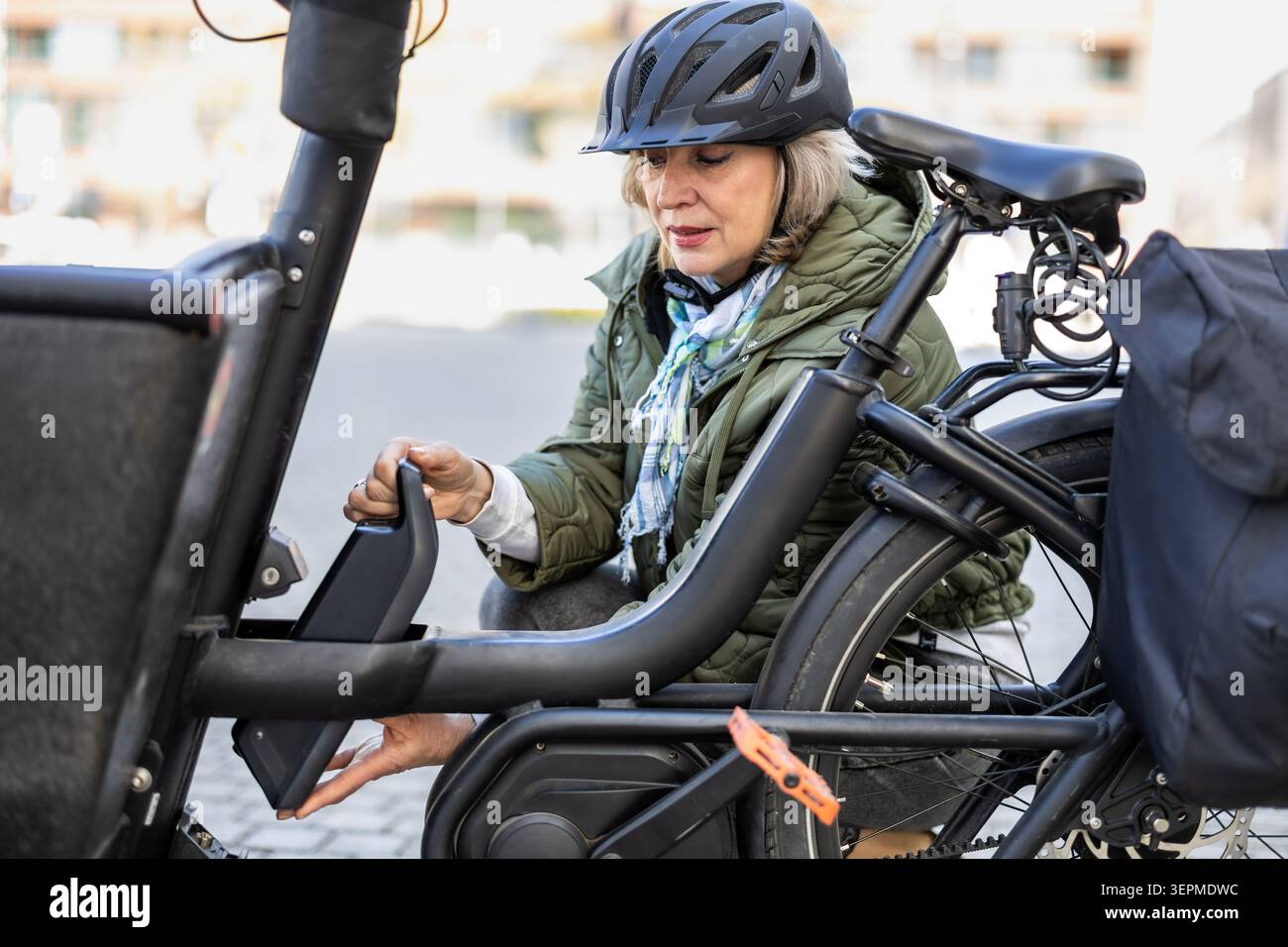 Donna matura che cambia la batteria su una bicicletta elettrica Foto Stock