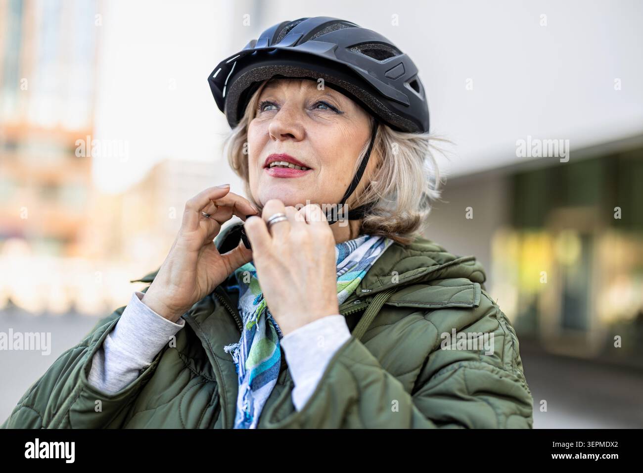 Donna anziana che adatta il casco da bicicletta all'aperto Foto Stock