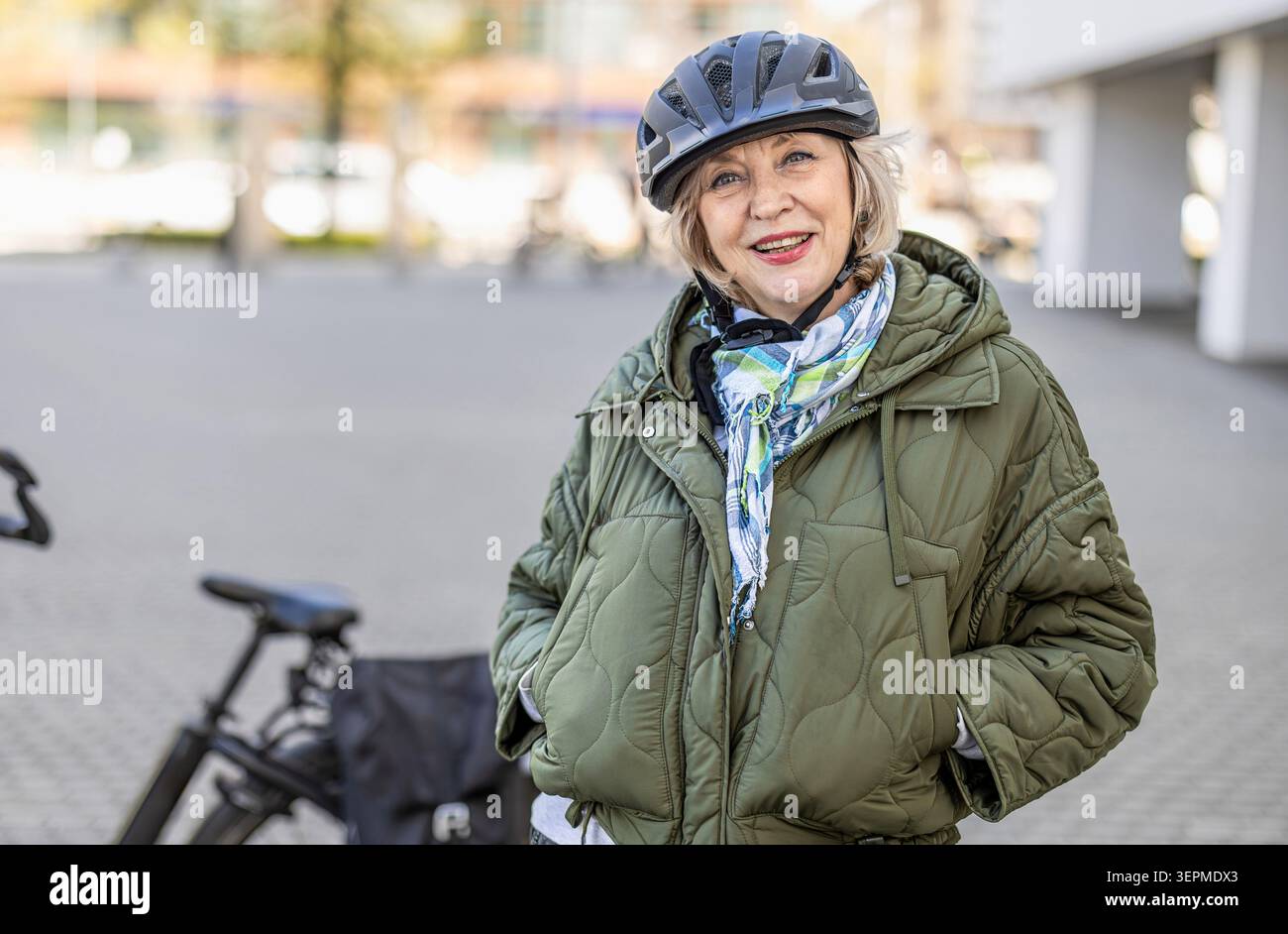 Donna anziana che indossa il casco mentre va in bicicletta in città Foto Stock