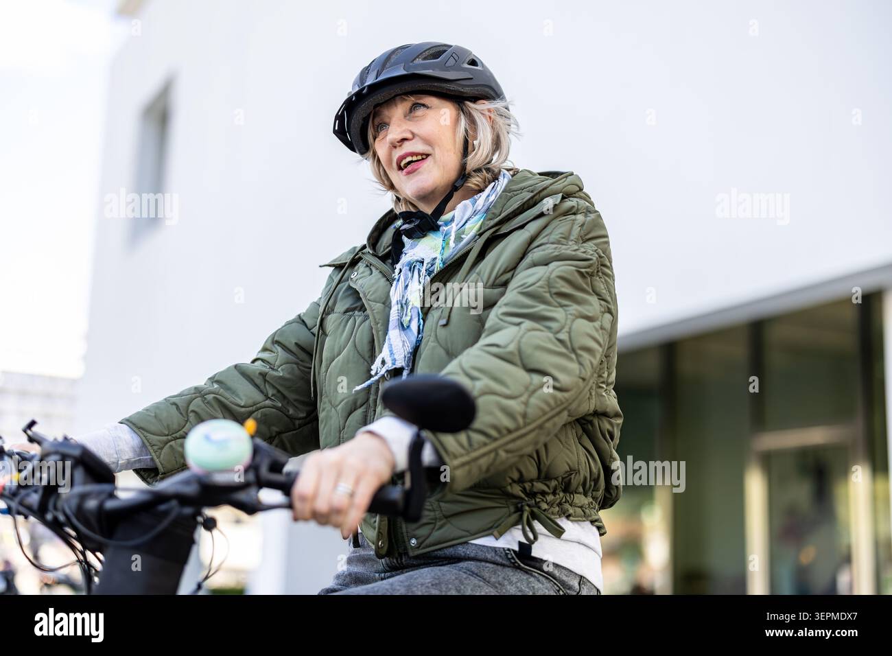 Donna anziana che indossa il casco mentre va in bicicletta in città Foto Stock