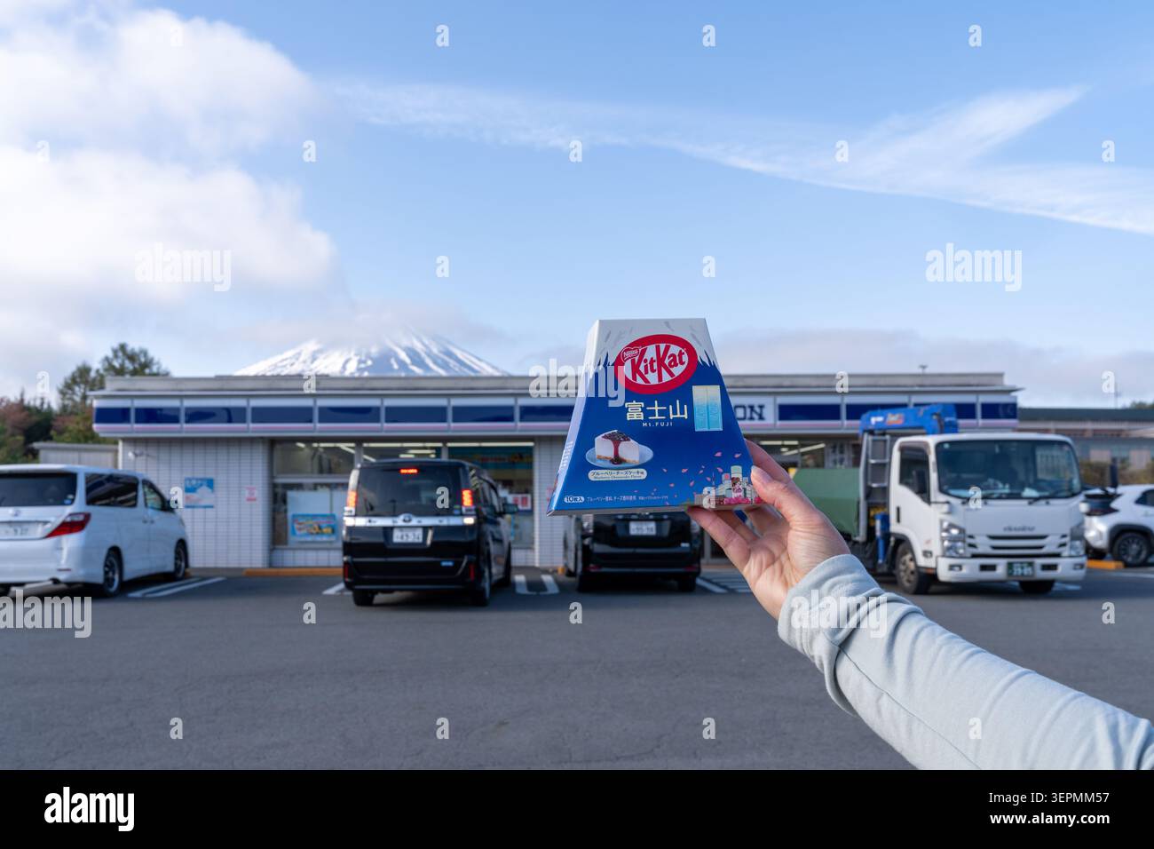 Yamanashi, Giappone - 16 aprile 2026: Famosa stazione Lawson Kawaguchiko con il Monte Fuji sullo sfondo, tenuta con una scatola di Kit Kats Foto Stock