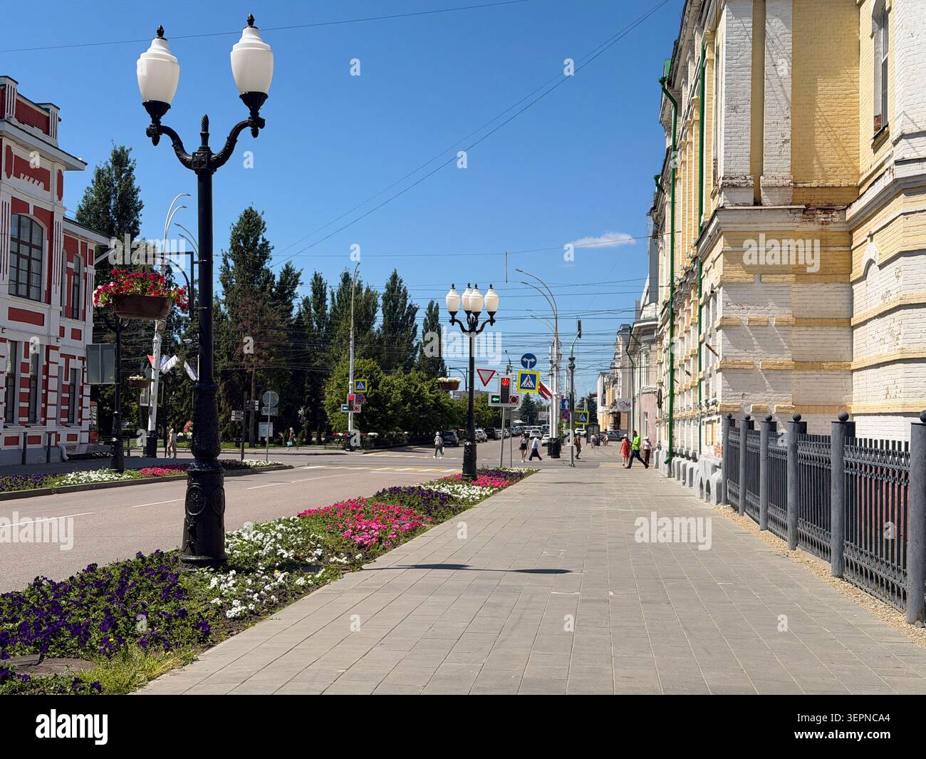 Tambov, Federazione Russa - 8 giugno 2026 Una strada soleggiata nel centro storico di Tambov con lampioni d'epoca, aiuole fiorite lungo una - Immagine stock catturata con smartphone