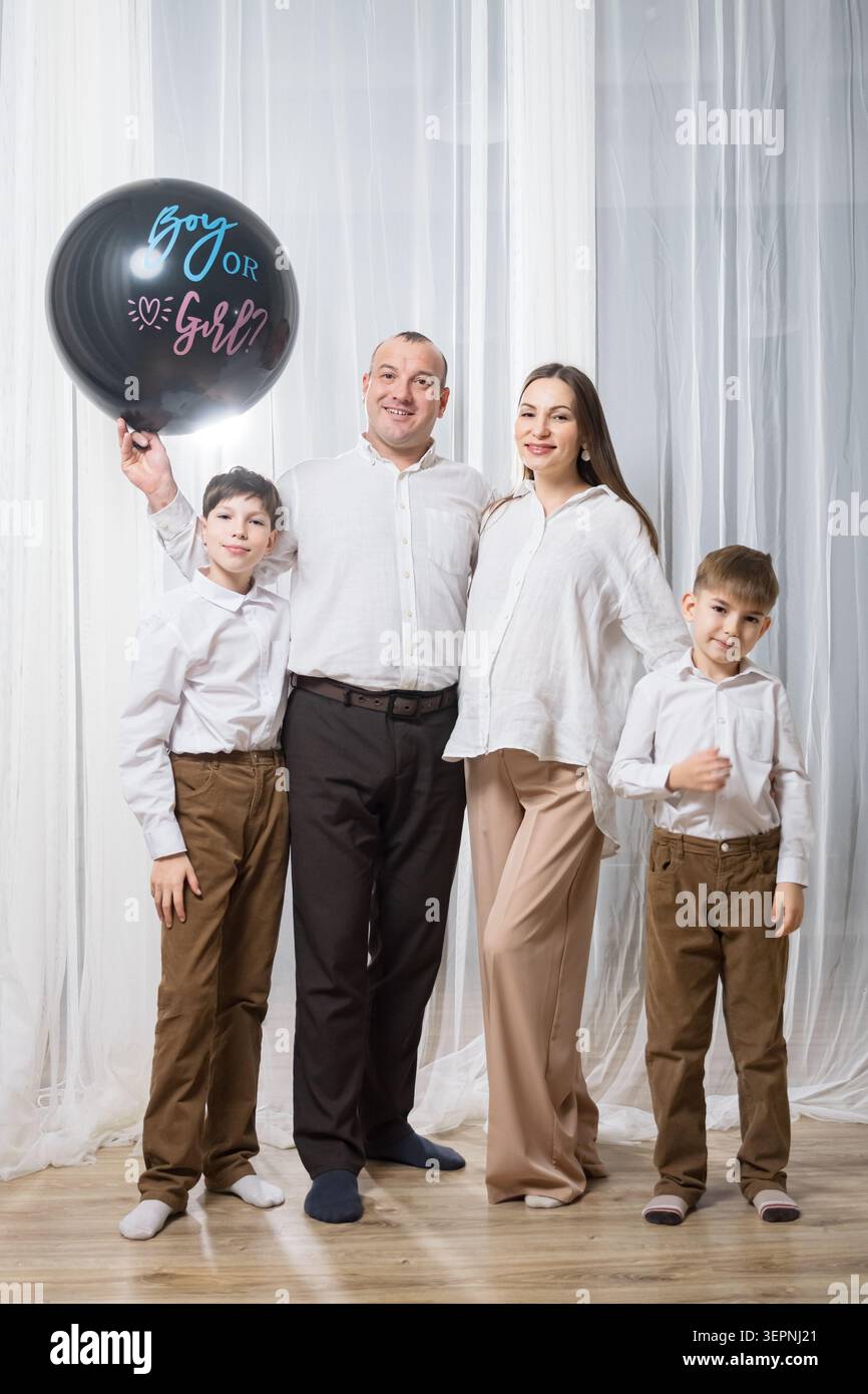 Famiglia caucasica in posa pallone da festa di genere, pallone nero opaco che legge ITS A Girl, genitori in abiti neutri, illuminazione sottile studio, drappeggiato Foto Stock