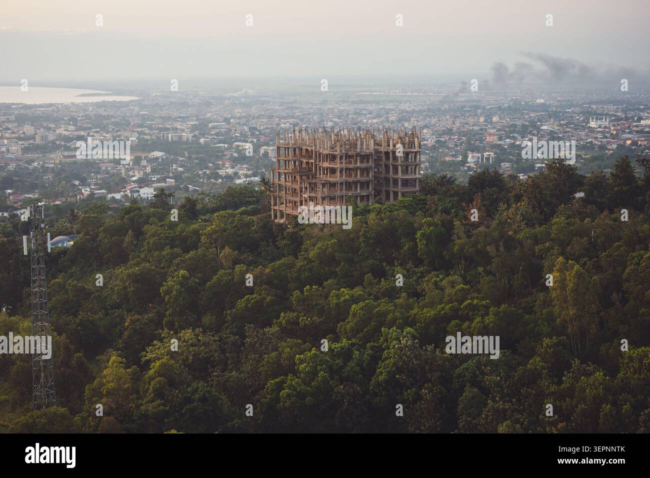 Un edificio in cemento a più piani incompiuto e abbandonato si trova circondato da una fitta foresta verde sulle colline che si affacciano sulla città di Bujumbura. Foto Stock
