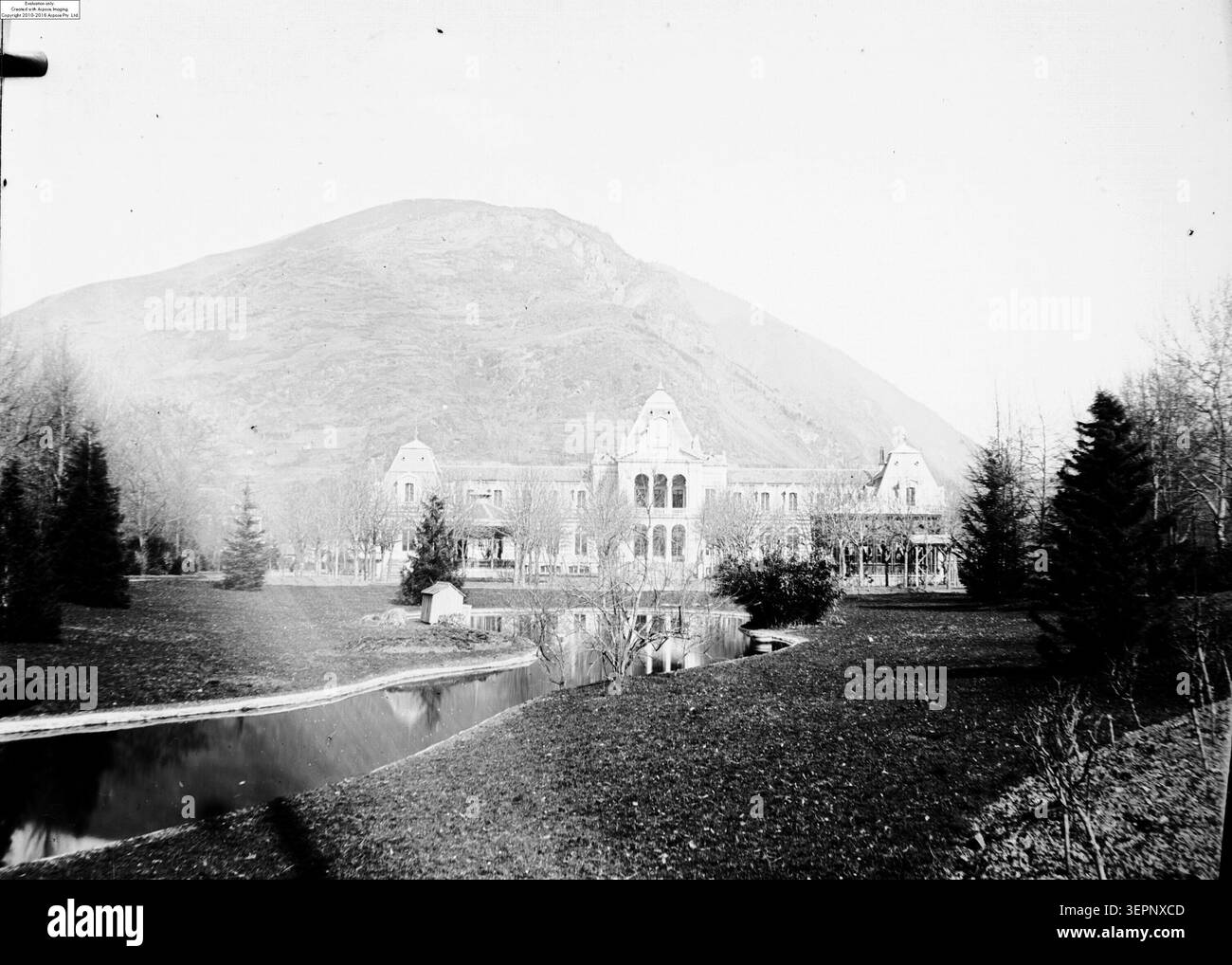 Eugène Trutat fotografa l'edificio del casinò di Bagnères-de-Luchon durante l'inverno, mostrando un parco paesaggistico con aiuole, alberi tra cui abeti e una facciata con balconi e dettagli architettonici. Foto Stock