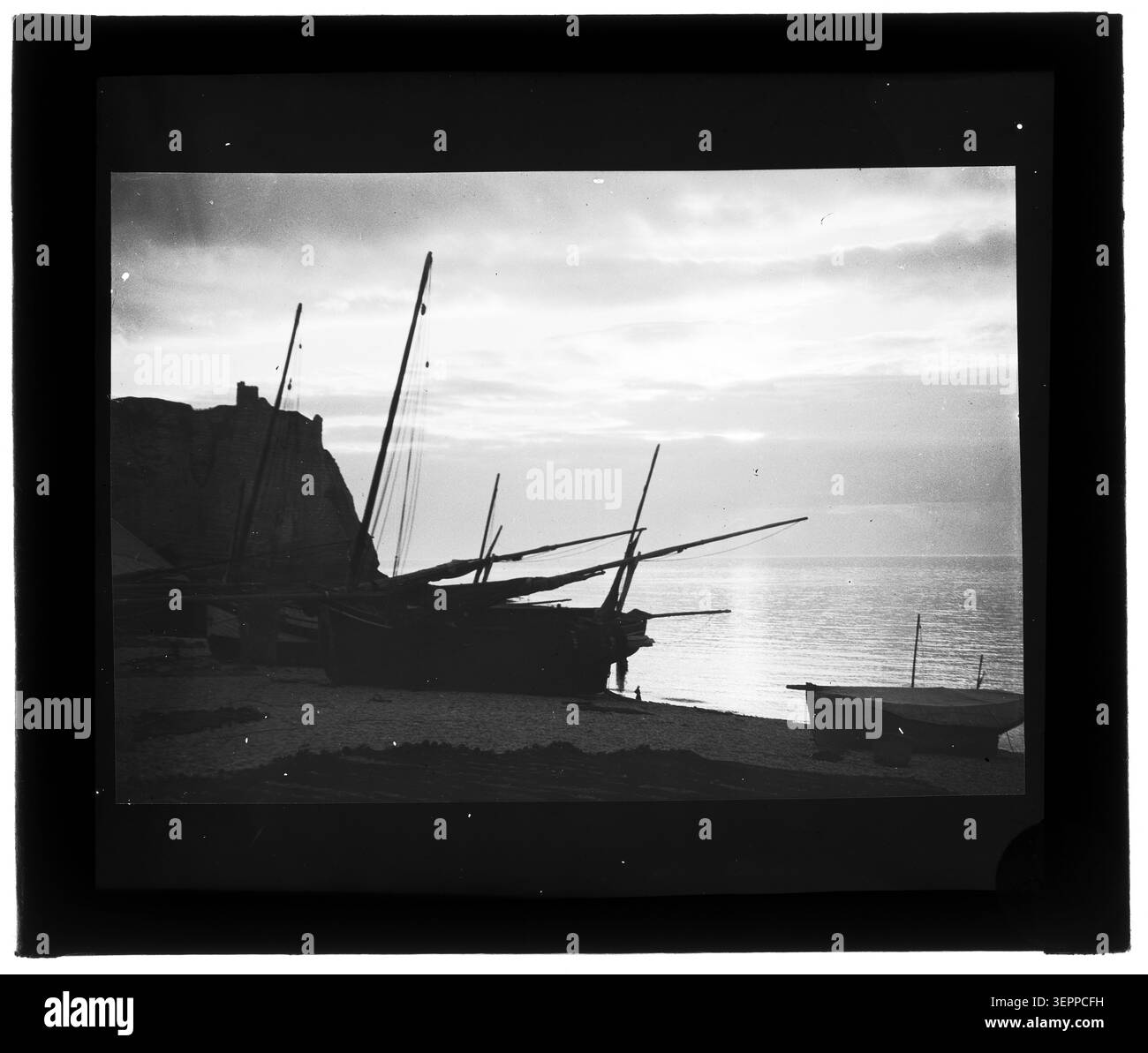 La stampa in gelatina d'argento presenta le barche ormeggiate lungo una costa al tramonto, registrando l'attività marittima costiera e la suggestiva luce serale sul mare all'interno di una struttura marina. Foto Stock