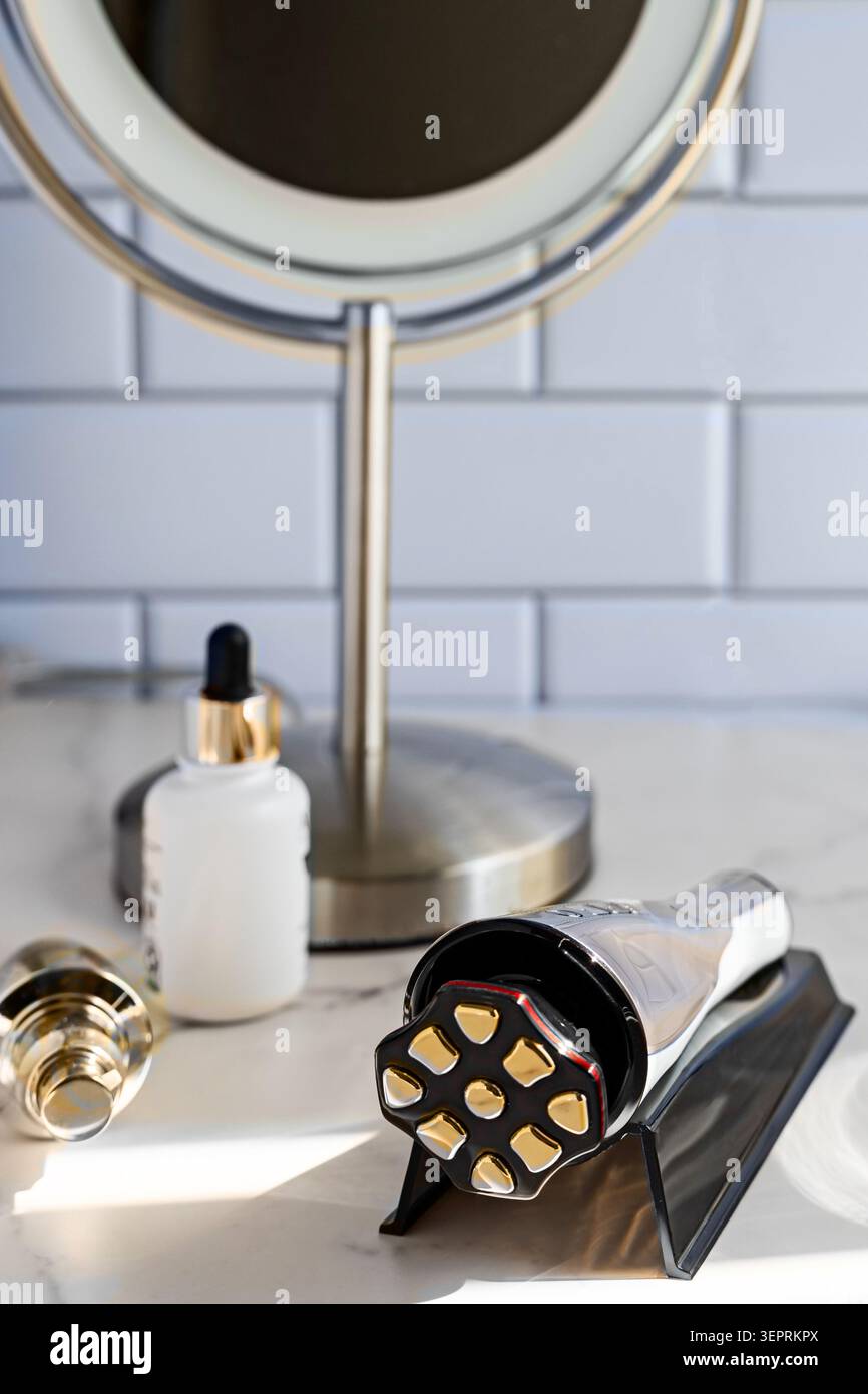 Moderno dispositivo antiinvecchiamento per il viso con bottiglia per la cura della pelle sul banco del bagno in marmo Foto Stock