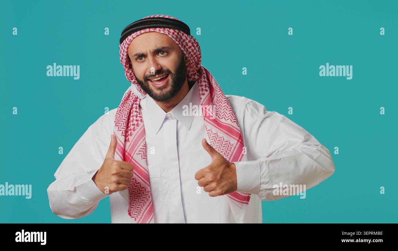 Di fronte alla macchina fotografica, il ragazzo del Medio Oriente dà il pollice in alto indicando il consenso e l'adempimento mentre è vestito con il consueto abbigliamento musulmano, giovane che indossa abiti arabi tradizionali, come simbolo. Foto Stock