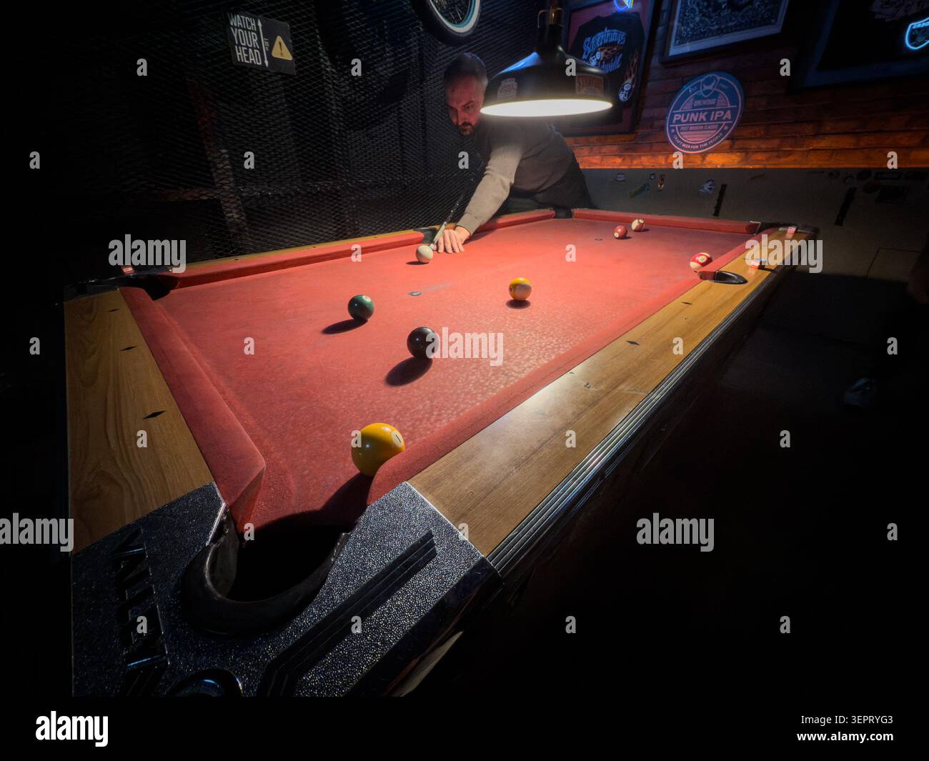 BELGRADO, SERBIA - 28 MARZO 2026: Uomo che gioca a biliardo su un tavolo da biliardo in feltro rosso in un bar poco illuminato, con palle da biliardo, bastoncino e illuminazione interna del pub Foto Stock