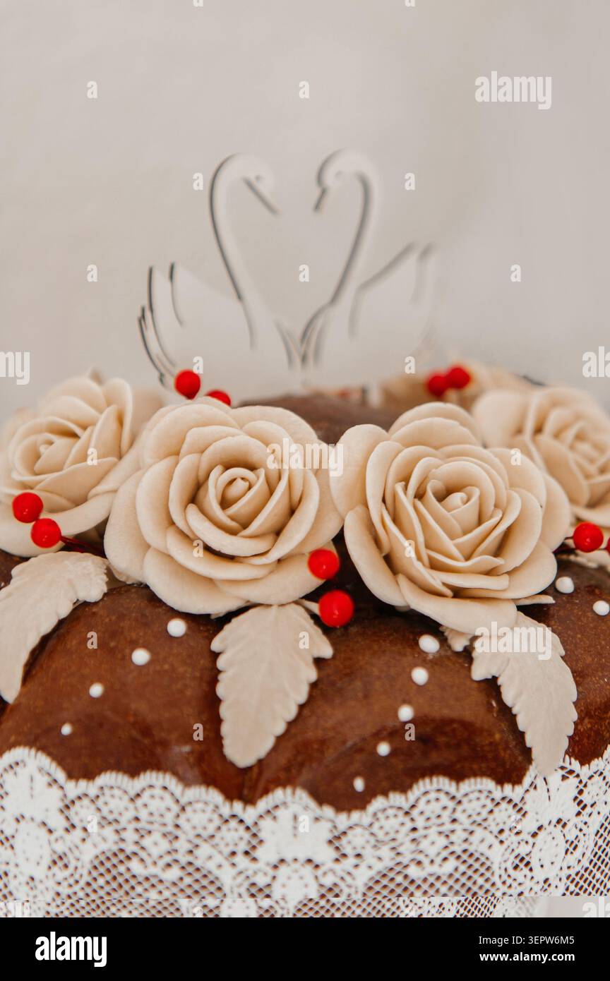Uno shot ravvicinato di un tradizionale pane da sposa splendidamente decorato, adornato con rose fondenti beige artigianali, piccoli frutti di bosco rossi e un elegante Foto Stock