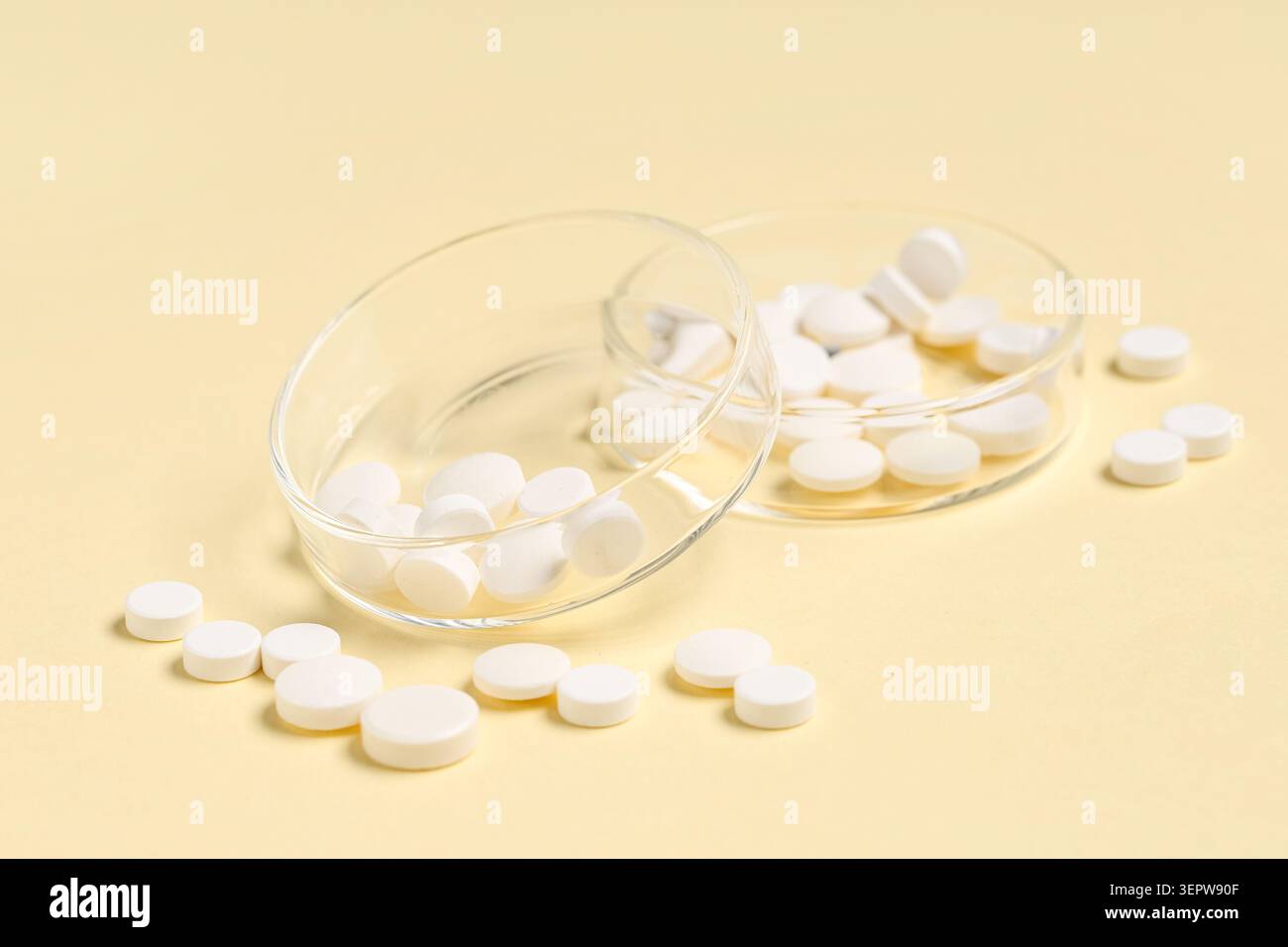 Pillole rotonde bianche in capsule di Petri di vetro e sparse su sfondo giallo medicina farmaceutica e assistenza sanitaria, la presentazione pulita sottolinea m Foto Stock