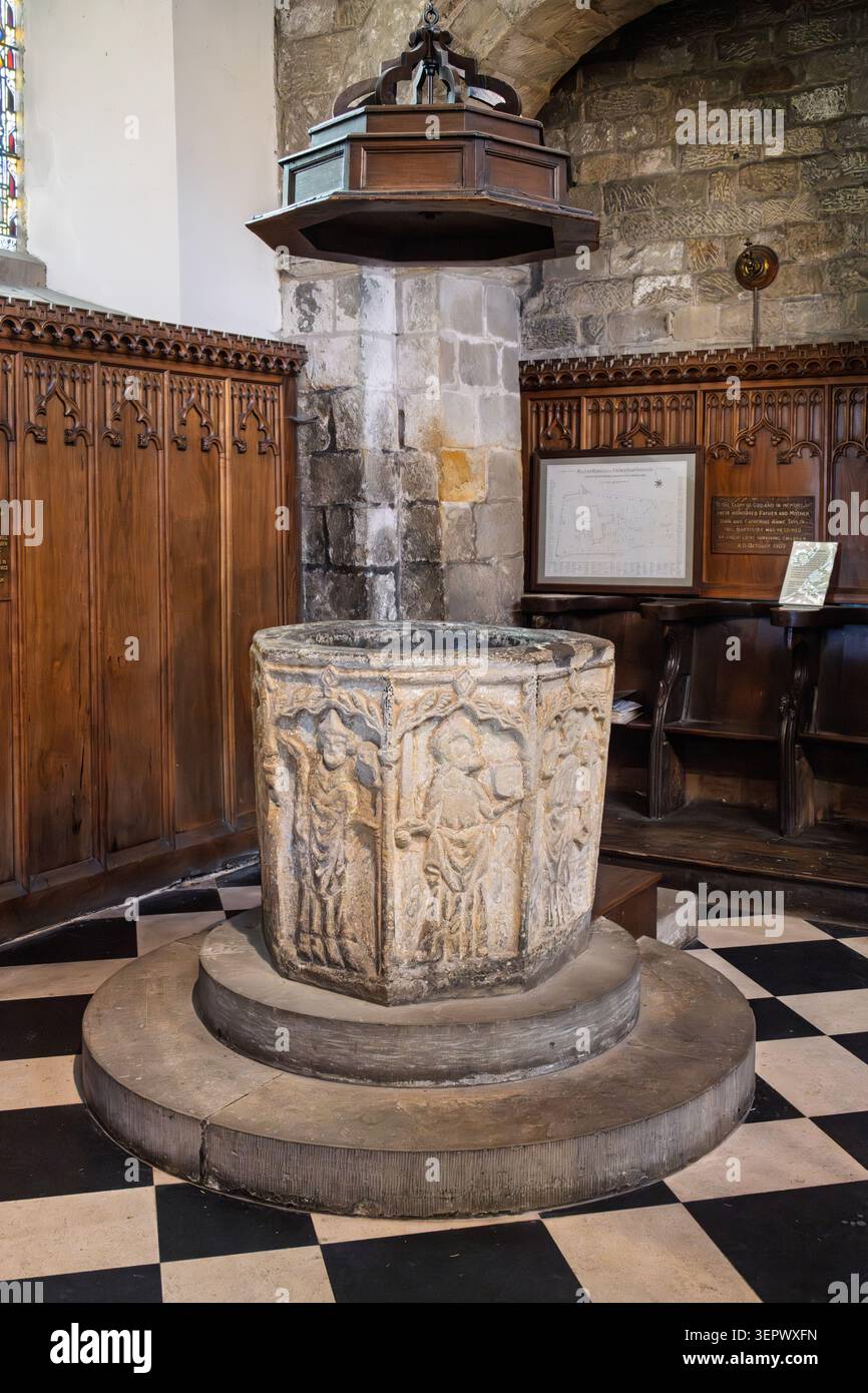 Il fonte battesimale ottagonale in pietra del XIV secolo scolpito con santi sotto una copertura lignea all'interno della Chiesa di Ognissanti a Bakewell Foto Stock