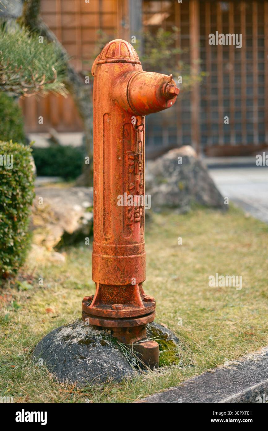 Vecchio idrante del fuoco di metallo arancione intemprato in piedi su una base di pietra in un'area giardino, Kyoto, Giappone Foto Stock