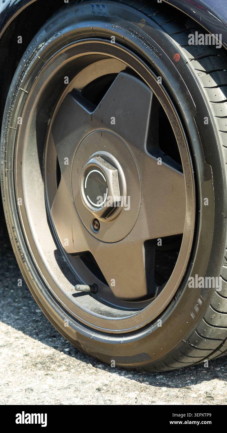 Cerchi automobilistici con razze a stella con finitura scura opaca e pneumatico a profilo basso. Stelo valvola pneumatico visibile, punto di bilanciamento rosso sulla parete laterale, e. Foto Stock