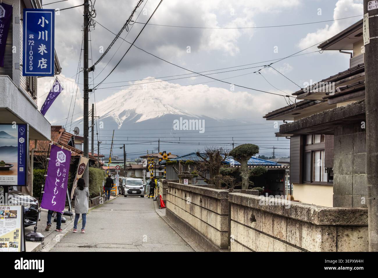 I pedoni camminano lungo una tranquilla strada di Funatsu con il Monte Fuji coperto di neve incorniciato davanti a Fujikawaguchiko, in Giappone. Foto Stock