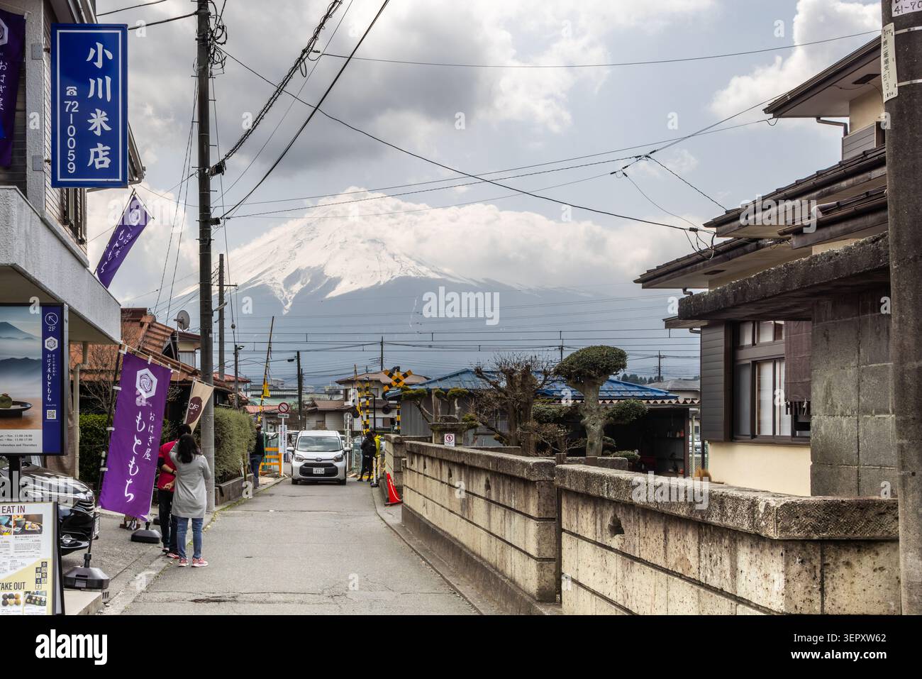 I pedoni camminano lungo una tranquilla strada di Funatsu con il Monte Fuji coperto di neve incorniciato davanti a Fujikawaguchiko, in Giappone. Foto Stock