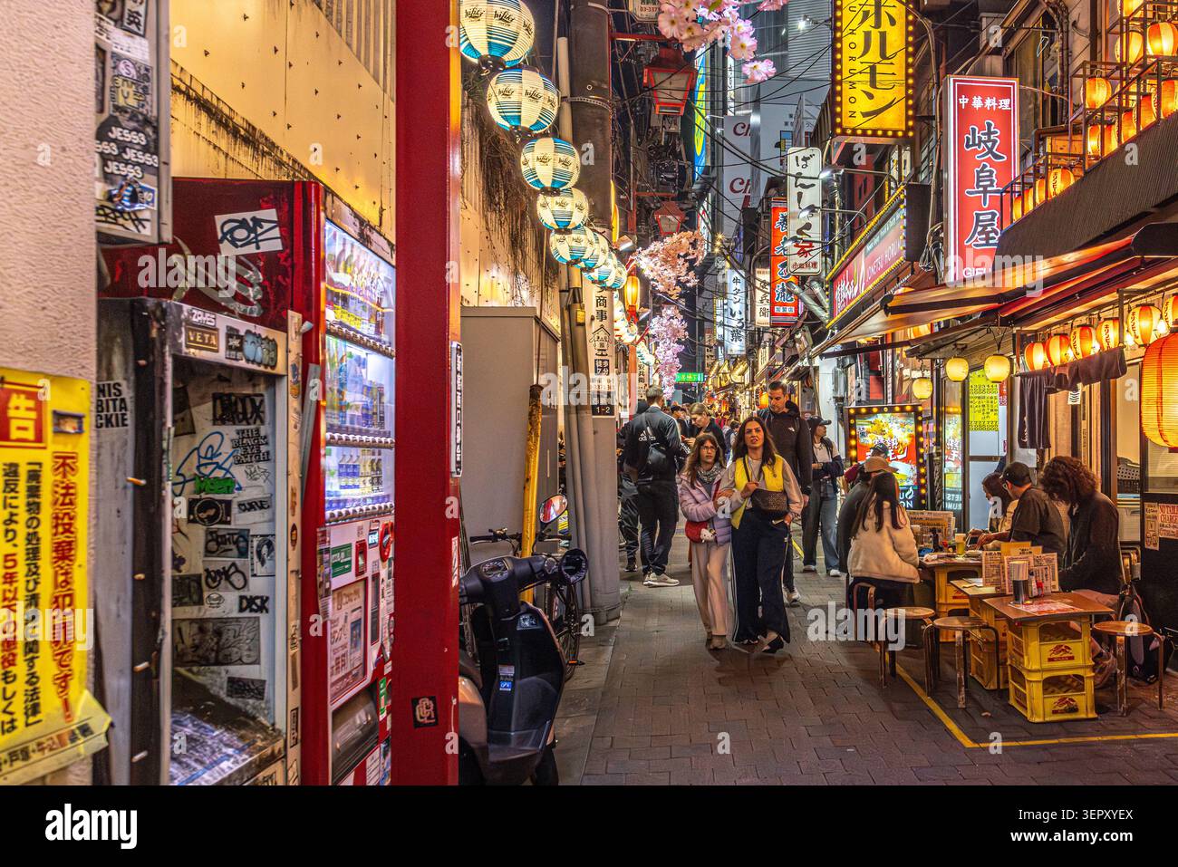 I visitatori passeggiano attraverso i vicoli illuminati dalle lanterne e i piccoli ristoranti di Shinjuku Omoide Yokocho di notte, Tokyo, Giappone. Foto Stock