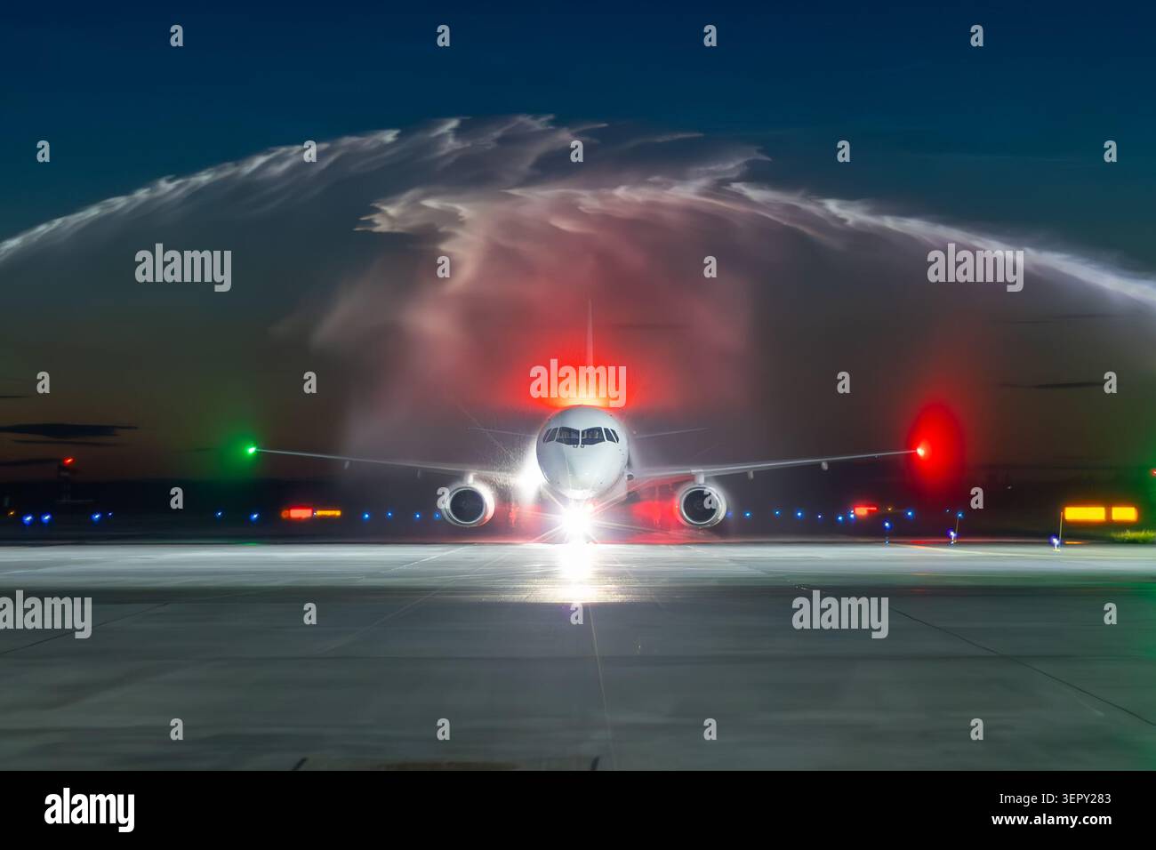 Vista frontale di un aereo passeggeri bianco che passa attraverso un arco d'acqua di notte. Prima visita in aereo all'aeroporto Foto Stock