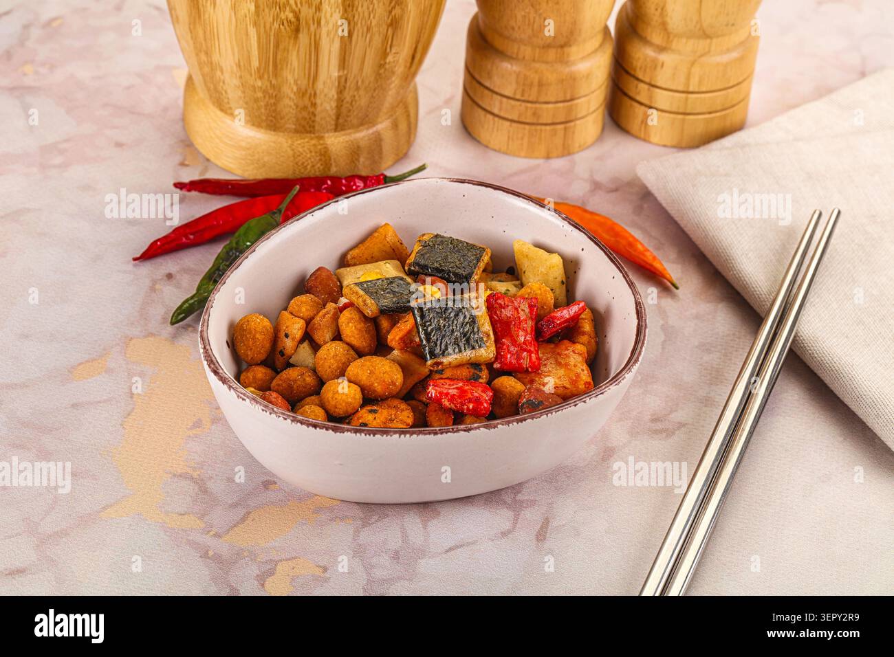 Uno shot ravvicinato di una ciotola riempita con uno spuntino speziato composto da alghe, arachidi, cracker colorati, accompagnati da peperoncini rossi, bacchette, ecc. Foto Stock