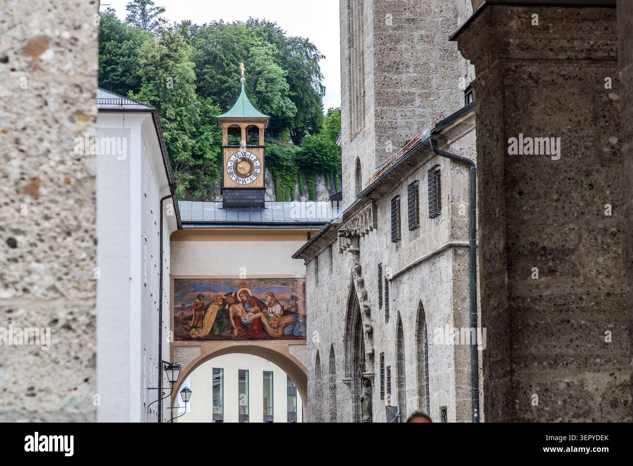 Una vista attraverso un arco nella città vecchia di Salisburgo verso una storica torre dell'orologio con una cupola di rame e una faccia dorata dell'orologio, nonché un affresco sulla facciata di un edificio; sulla destra, l'imponente parete esterna della Chiesa francescana. La città vecchia di Salisburgo è un sito patrimonio dell'umanità dell'UNESCO dal 1997. Salisburgo, Austria Foto Stock