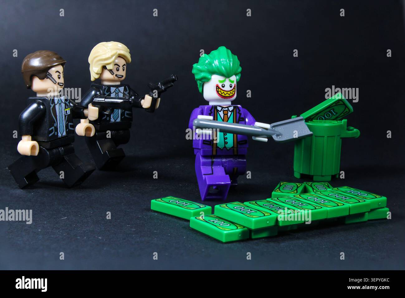 LEGO Joker, cercando di rubare denaro usando una pala, mentre due agenti gli puntano un'arma contro. Foto Stock