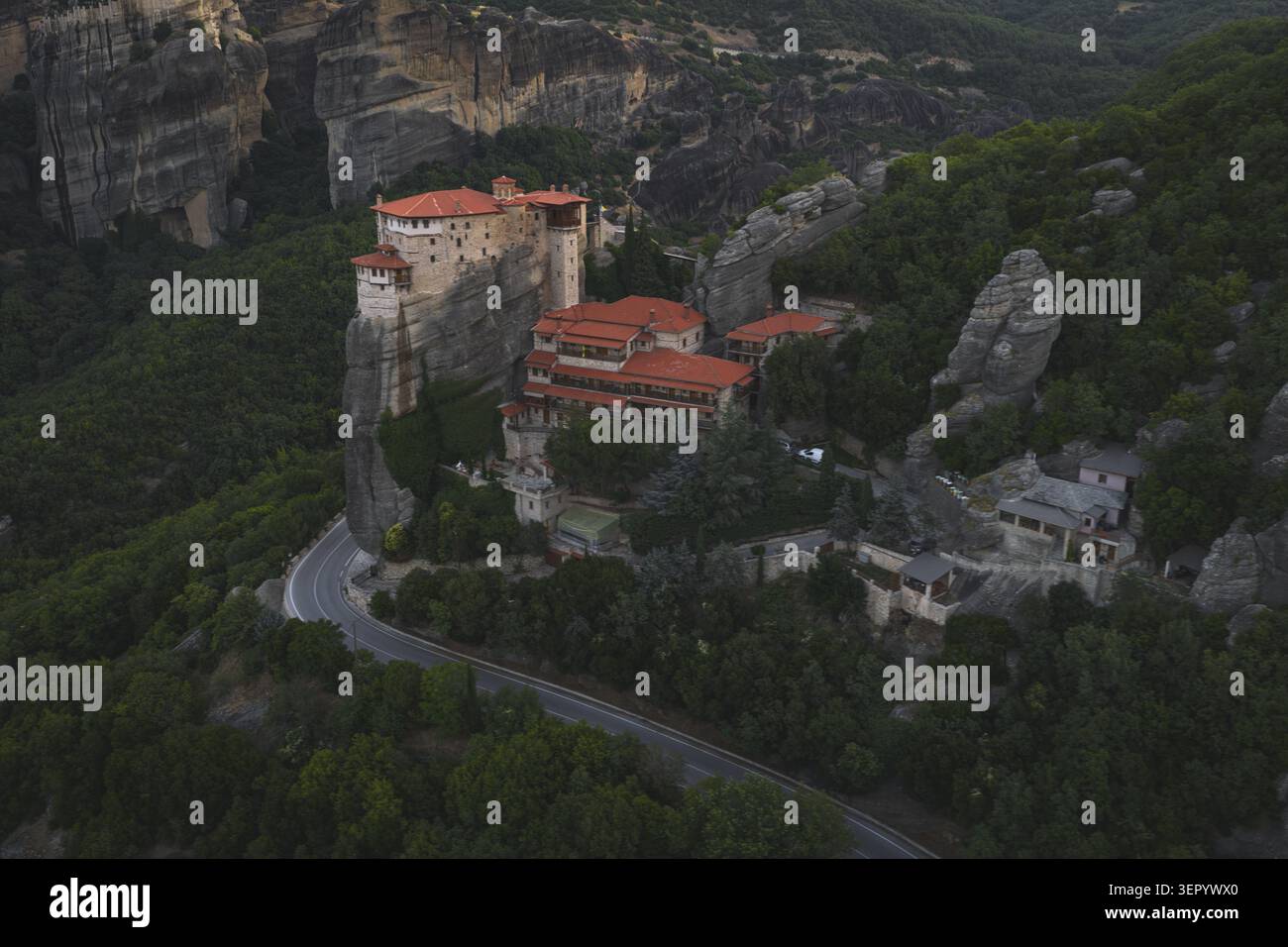 Vista aerea del monastero Rousanou a Meteora con i suoi tetti di tegole rosse arroccati su una ripida colonna rocciosa circondata da una fitta foresta verde a Trikala, Foto Stock