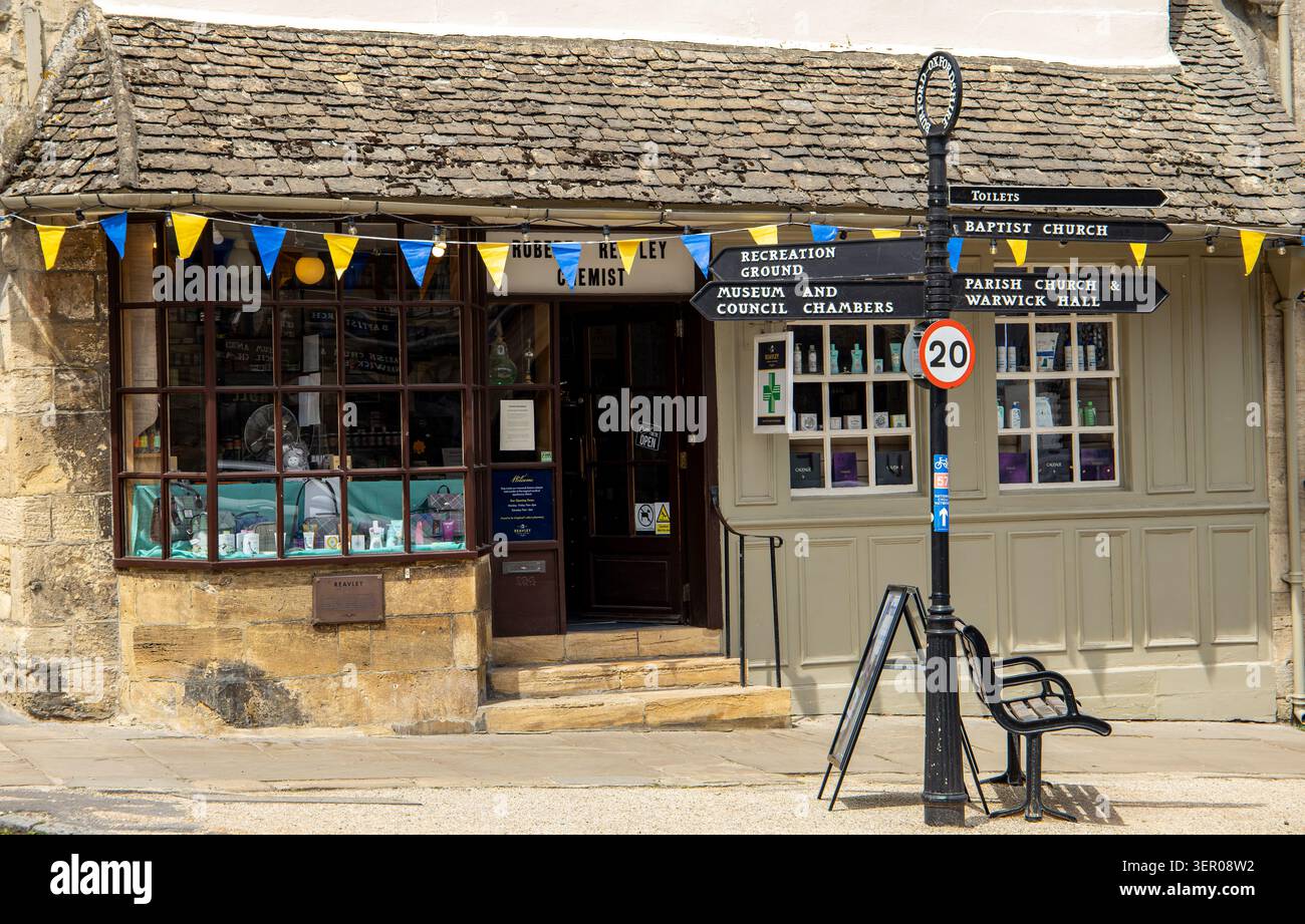 Storico negozio di farmacia in un tradizionale villaggio inglese in pietra con cartelli direzionali e decorazioni a Burford, Oxfordshire Foto Stock