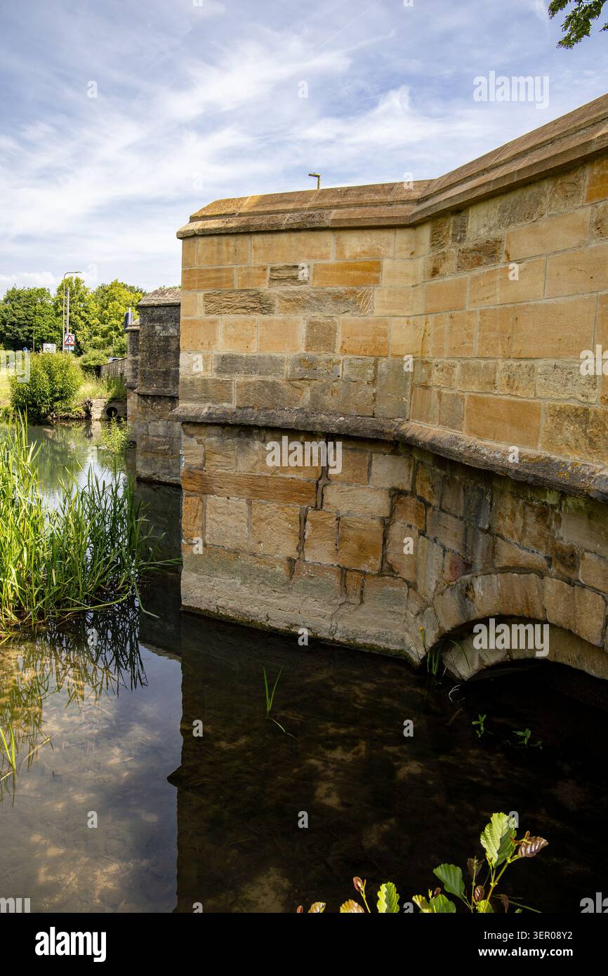 Dettaglio di un vecchio arco di ponte in pietra arenaria che attraversa un fiume in una giornata luminosa nella campagna di Burford Oxfordshire Foto Stock