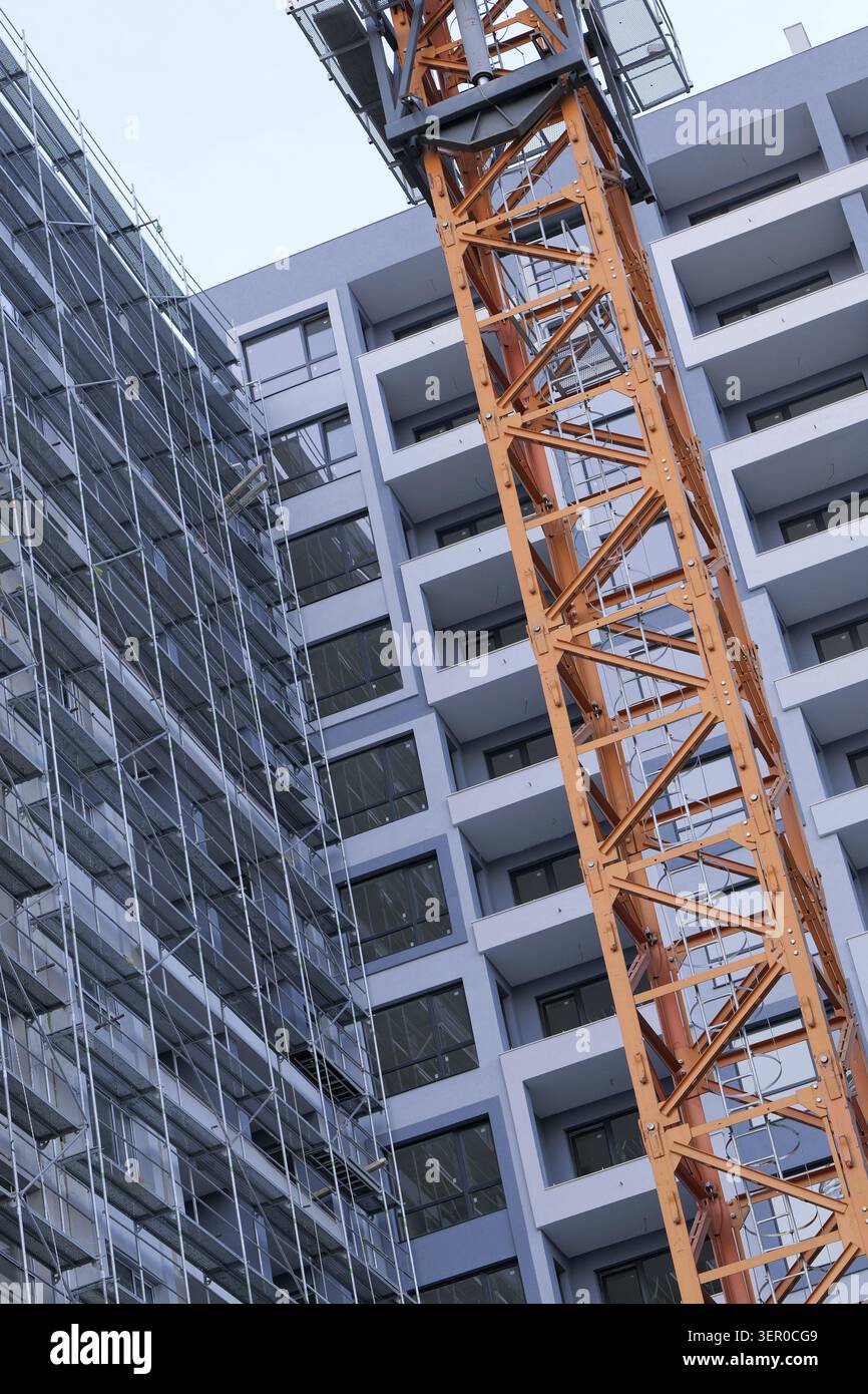 Gru a torre che opera accanto a un edificio residenziale in costruzione, con impalcature e elementi di design moderni, che illustrano lo sviluppo urbano Foto Stock