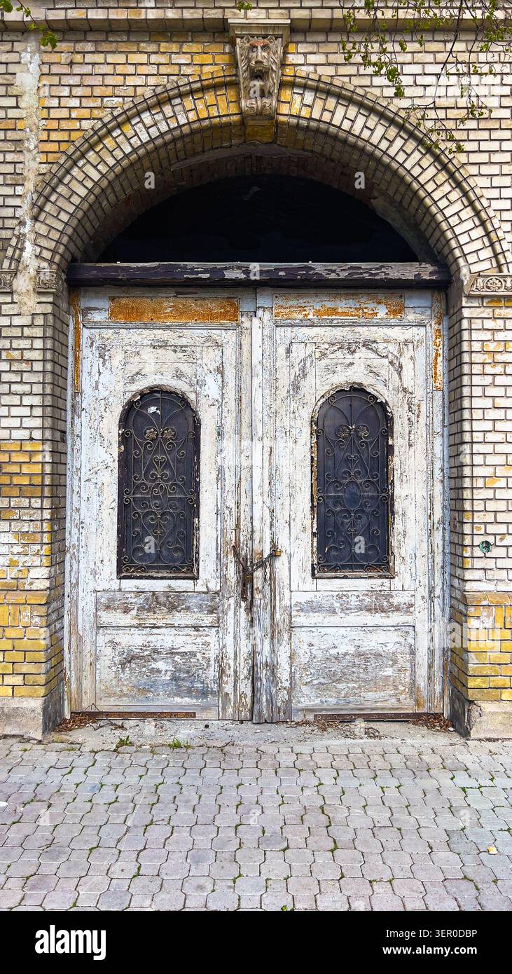 Vecchia porta d'ingresso con finestre decorative in ferro e facciata in mattoni, dettagli storici dell'edificio, immagine verticale - Immagine stock catturata con smartphone