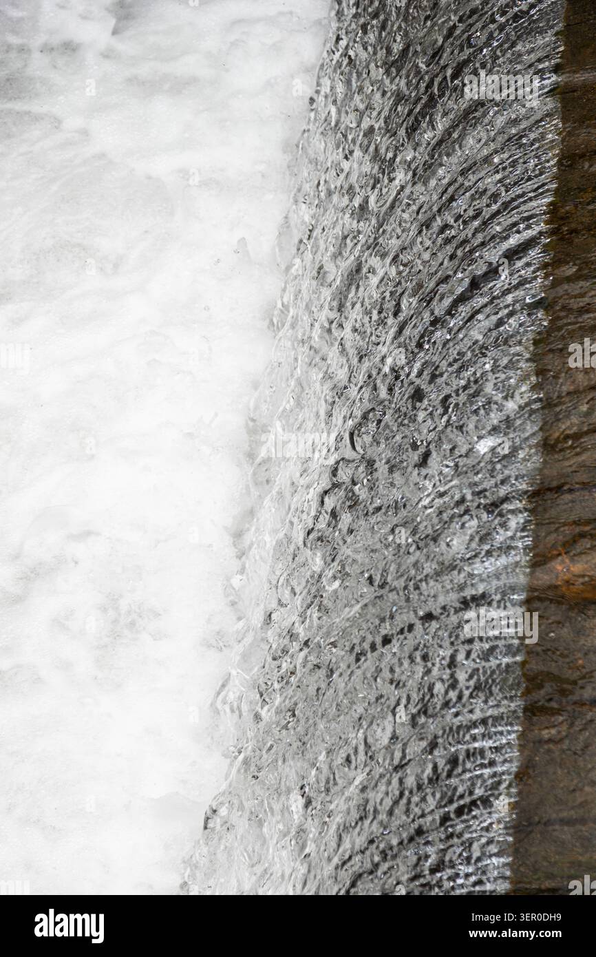 Vista verticale dettagliata dell'acqua affilata che scorre oltre una soglia di pietra in schiuma bianca vorticosa. Foto Stock