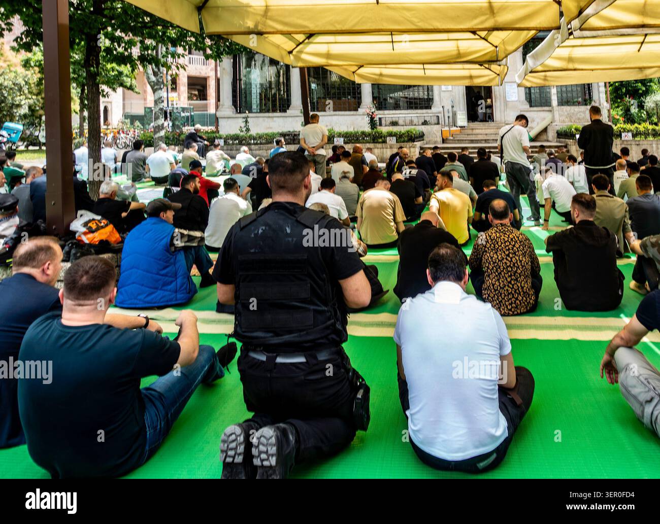Gli uomini musulmani si sono riuniti per la preghiera all'aperto del venerdì su tappeti verdi sotto grandi ombrelli beige accanto alla moschea et'hem Bey a Tirana, Albania. Foto Stock