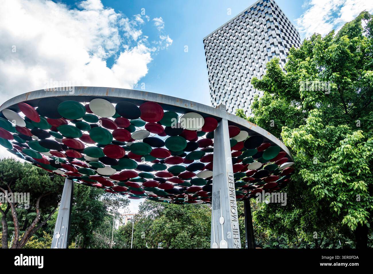 La struttura a baldacchino del Monumento dell'amicizia con il moderno grattacielo Plaza Hotel sullo sfondo sotto un cielo blu a Tirana, Albania. Foto Stock