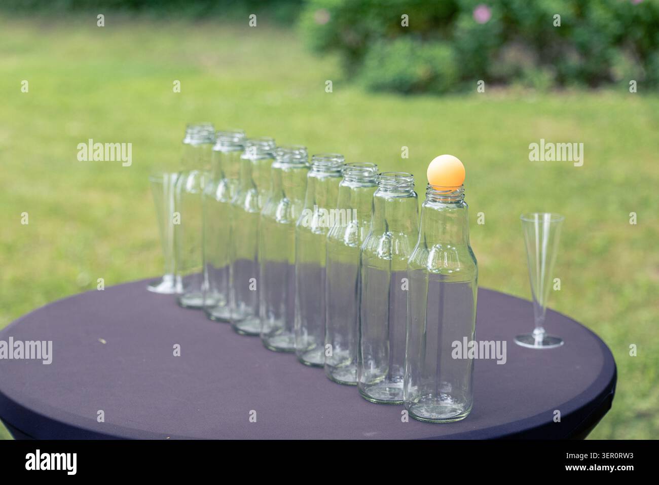 Gioco di sfida all'aperto con una palla da ping pong posta su una fila di bottiglie di vetro. Una linea retta di bottiglie vuote Foto Stock