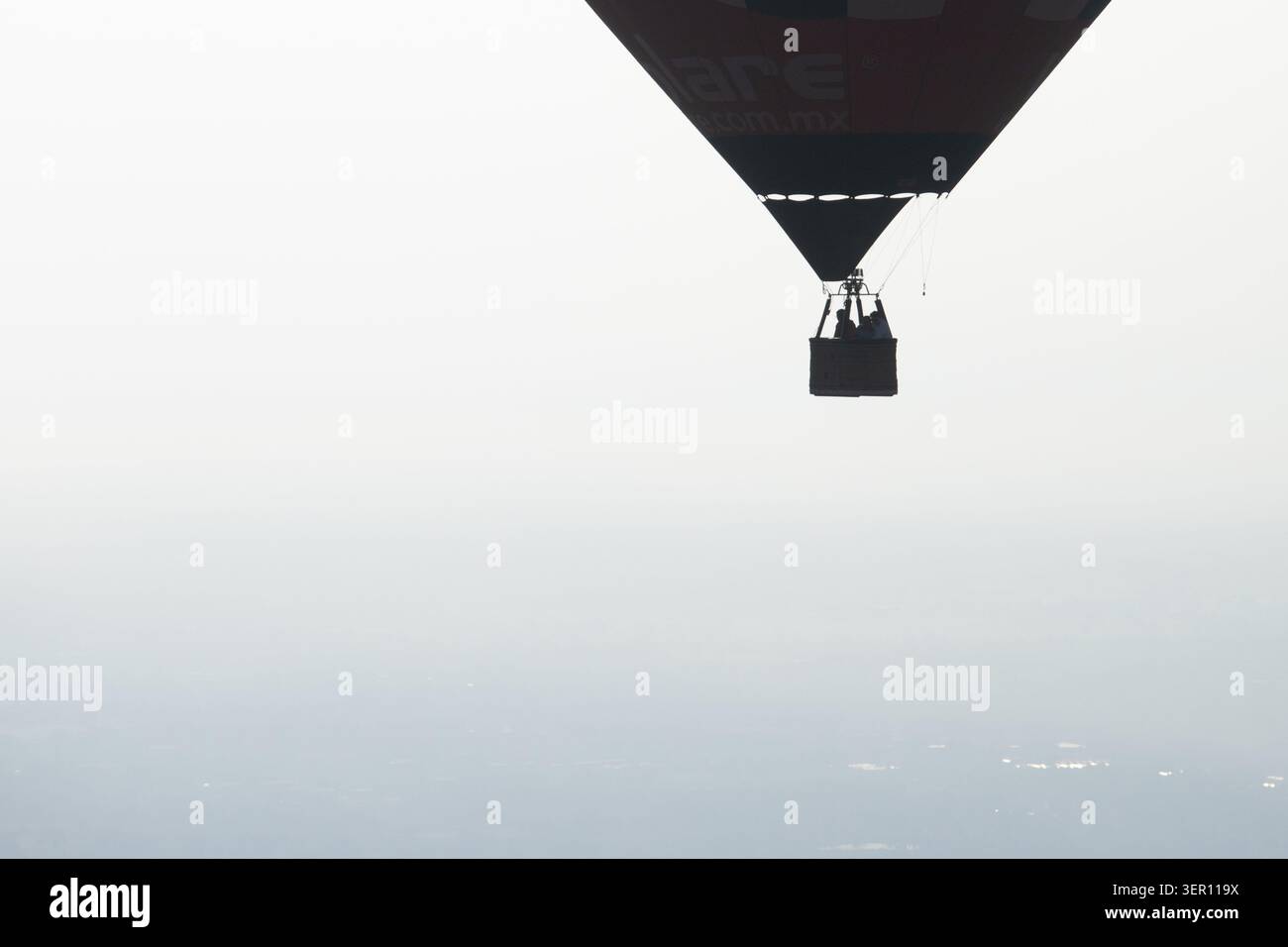 Mongolfiera con i passeggeri in un cesto sagomato contro un cielo pallido e nebbioso, vista aerea minimalista con spazio fotocopie Foto Stock