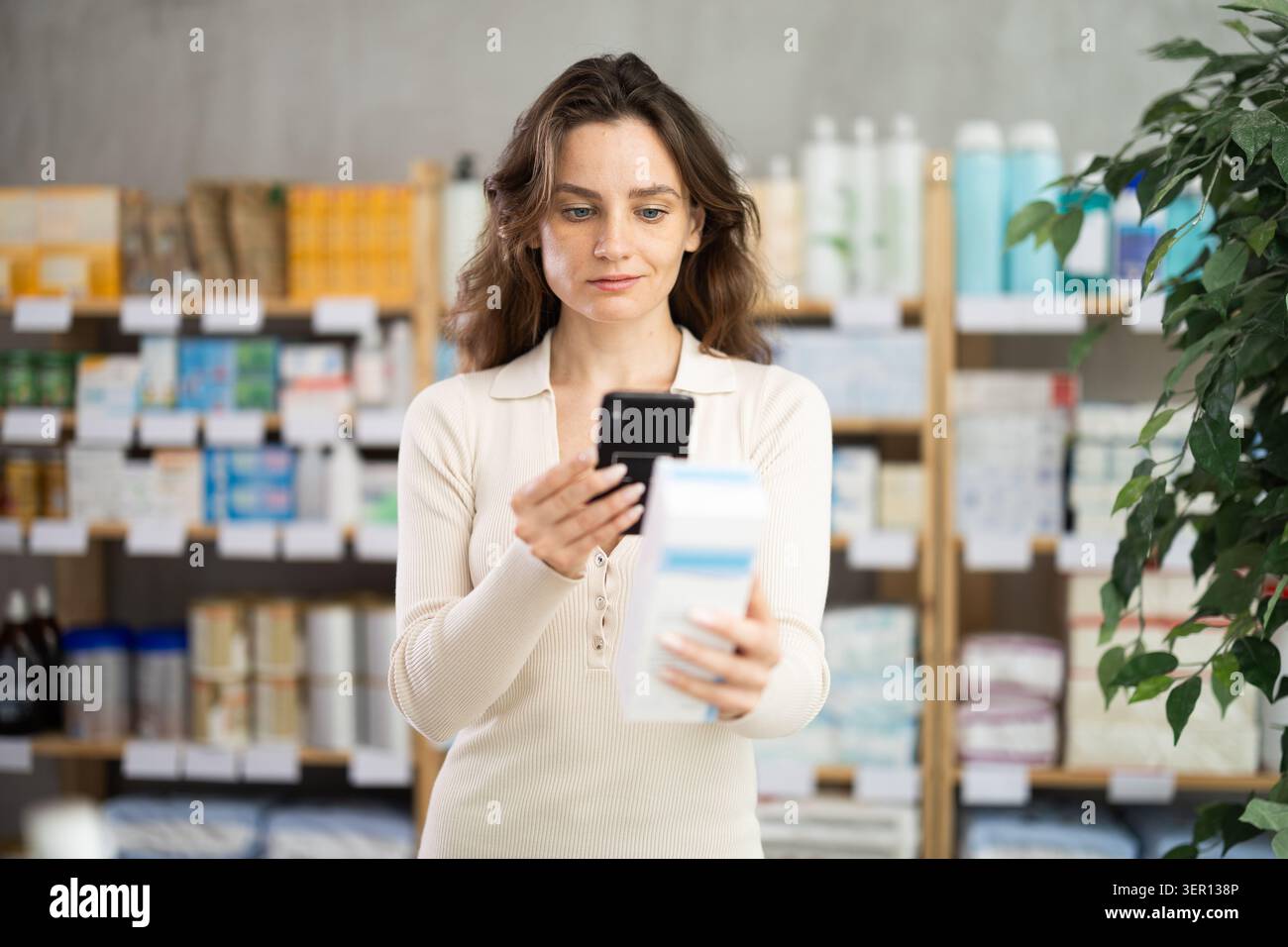 Donna in abiti estivi scansiona il codice sulla confezione della crema per controllare la data di scadenza Foto Stock
