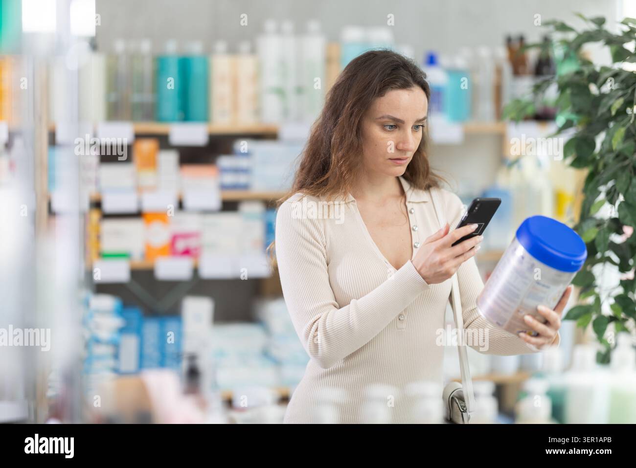 La donna che acquista abiti estivi scansiona il codice QR sull'etichetta del cibo per i bambini piccoli utilizzando lo smartphone Foto Stock