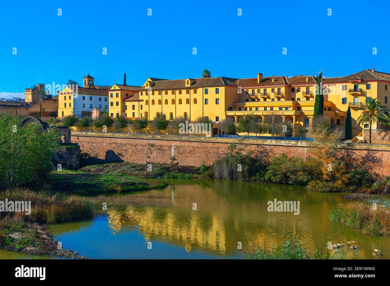 Storico lungofiume di Cordova, Spagna, con edifici gialli che si riflettono sul fiume Guadalquivir. Antico mulino ad acqua di Albolafia vicino alle mura della città Foto Stock