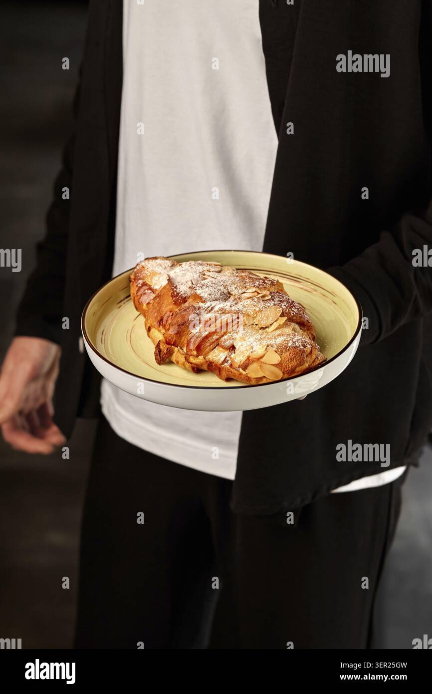 Panettiera che presenta un delizioso croissant alle mandorle, con la crosta dorata e la delicata spolveratura di zucchero a velo Foto Stock