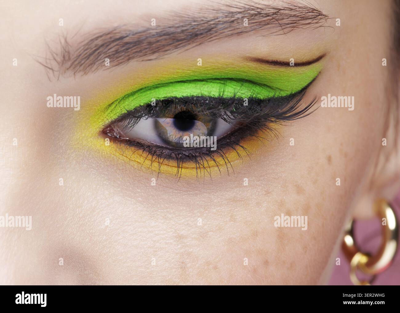 Primo piano macro di occhio umano femminile. Donna con un trucco di bellezza per il viso di moda. Ragazza con ombre verdi e gialle agli occhi Foto Stock