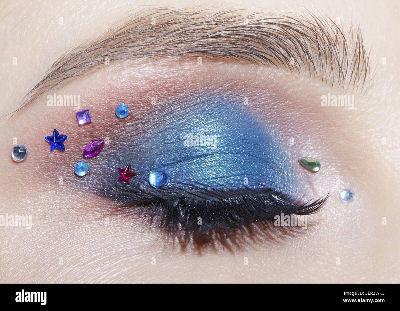 Foto macro di primo piano di un occhio umano femminile chiuso con ombre blu e strass. Donna con trucco naturale per la sera Foto Stock