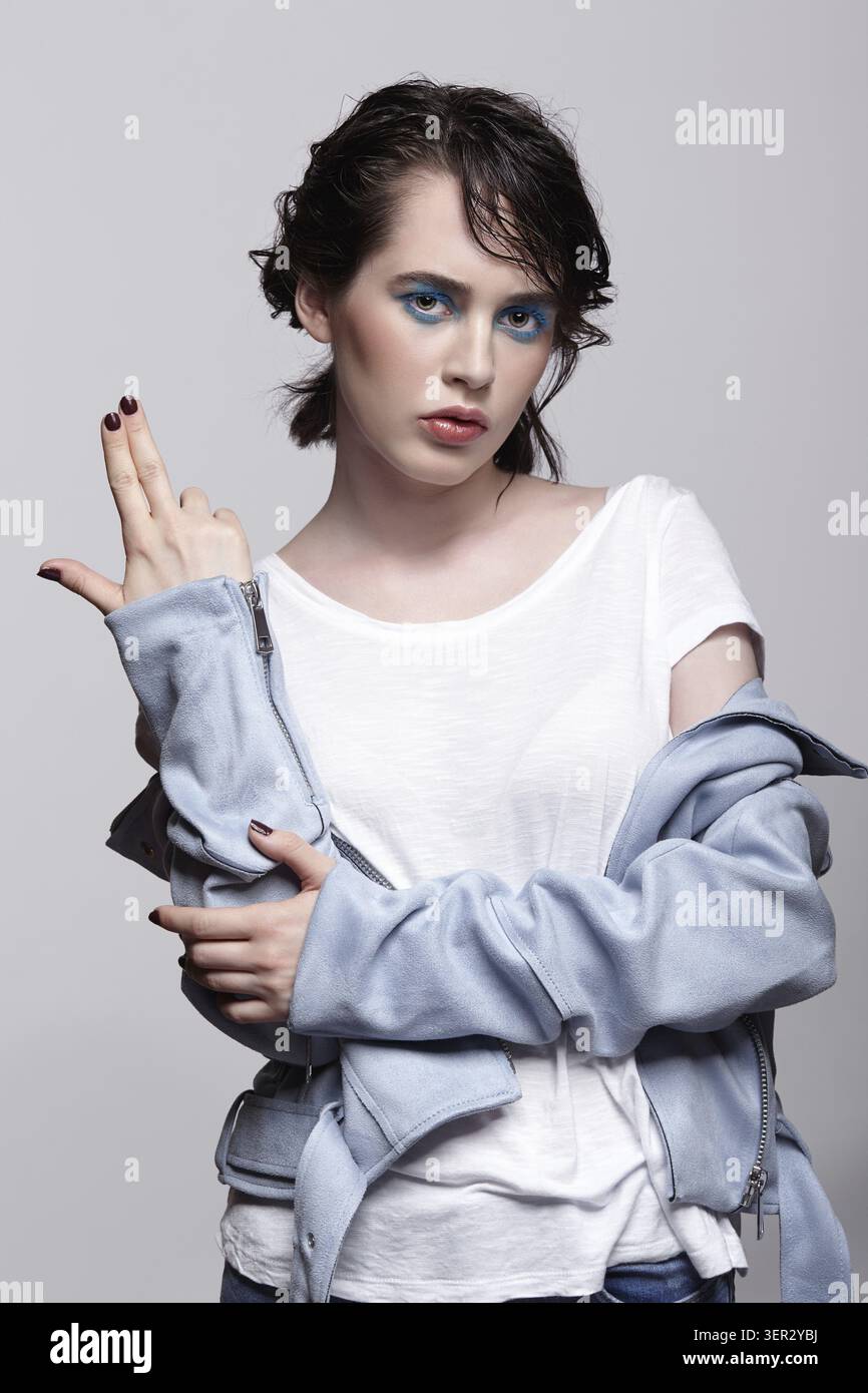 Ritratto di donna in giacca blu con le dita verso l'alto. Donna con inusuale bellezza trucco e capelli bagnati. Ragazza con una pelle perfetta, verde pistacchio occhi colore Foto Stock