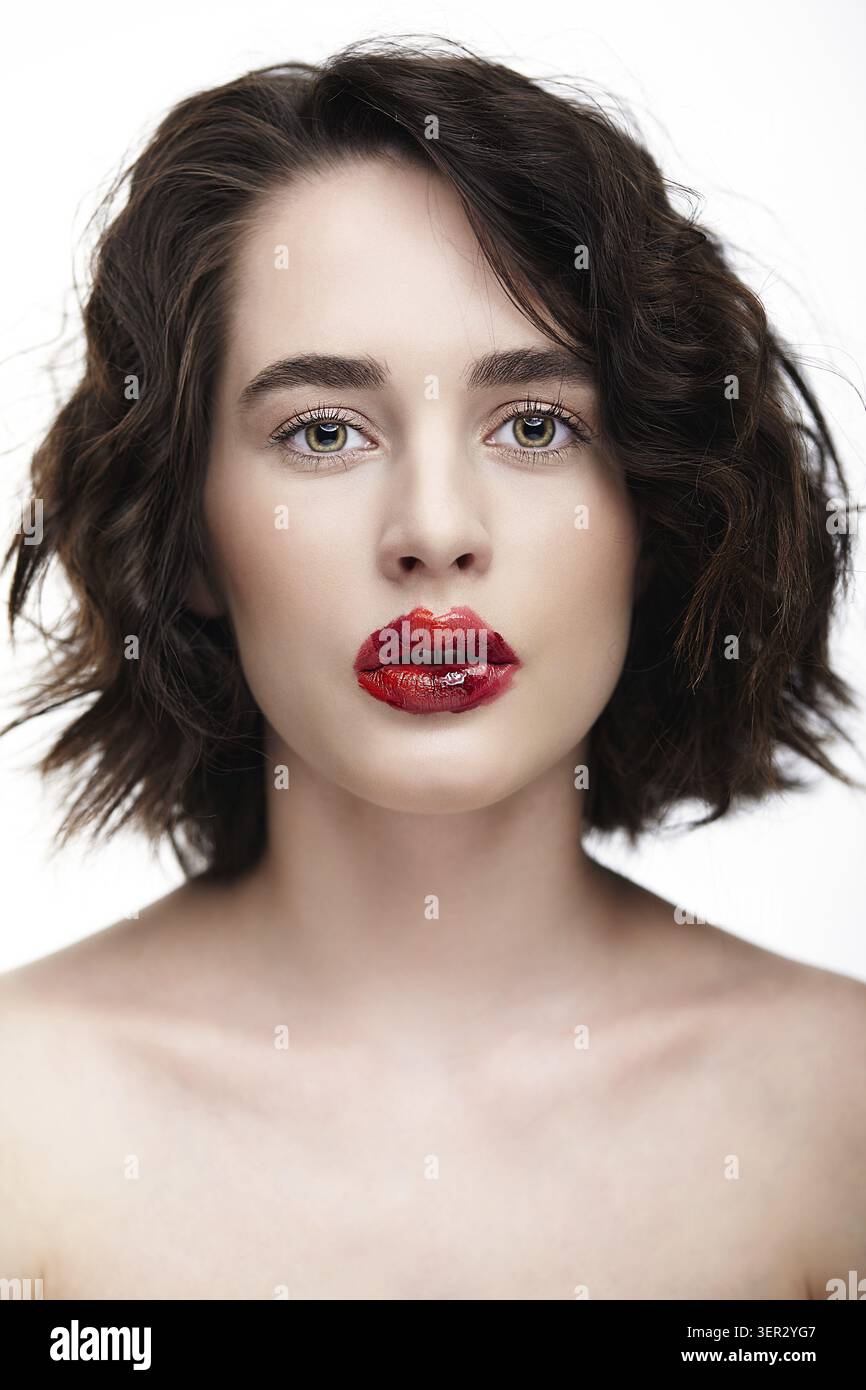 Ritratto del volto femminile. Donna mezza faccia con trucco di bellezza insolito. Ragazza dalla pelle perfetta, occhi verdi color pistacchio e trucco con labbra rosse scarlatte Foto Stock